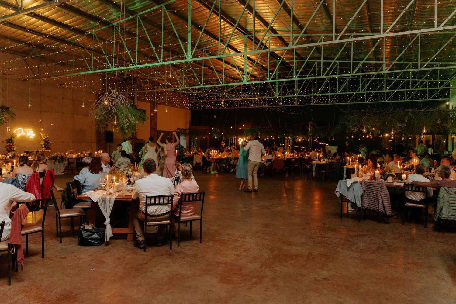 Large industrial warehouse venue set up for a wedding reception with tables and string lights overhead.