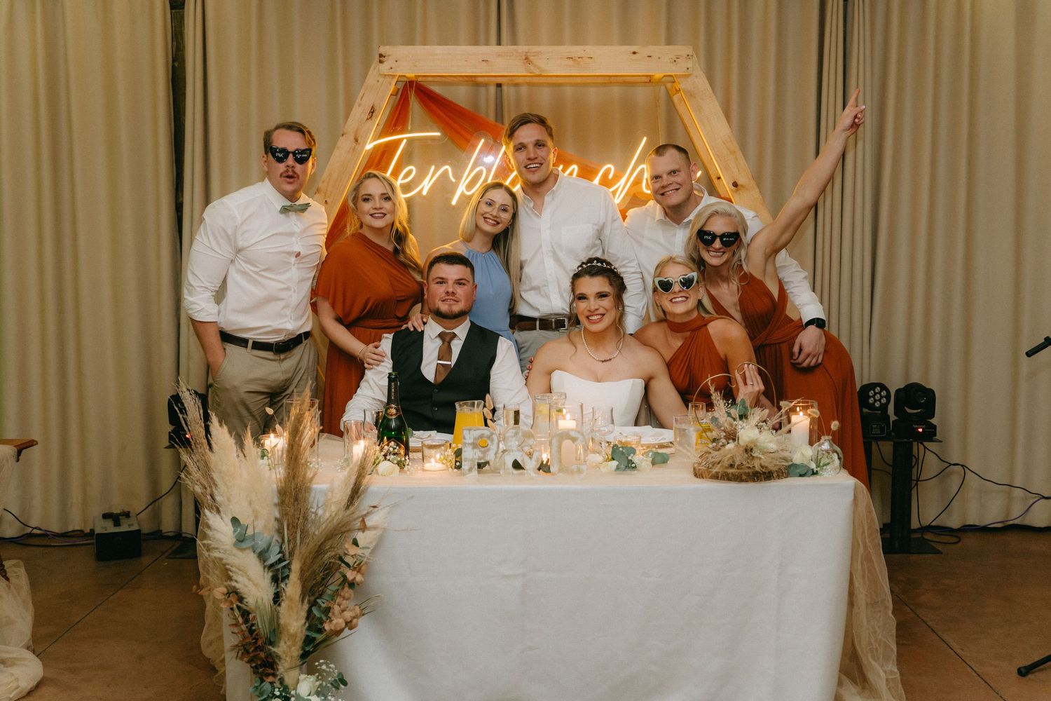 Wedding reception head table decorated with lights and signage for celebration.