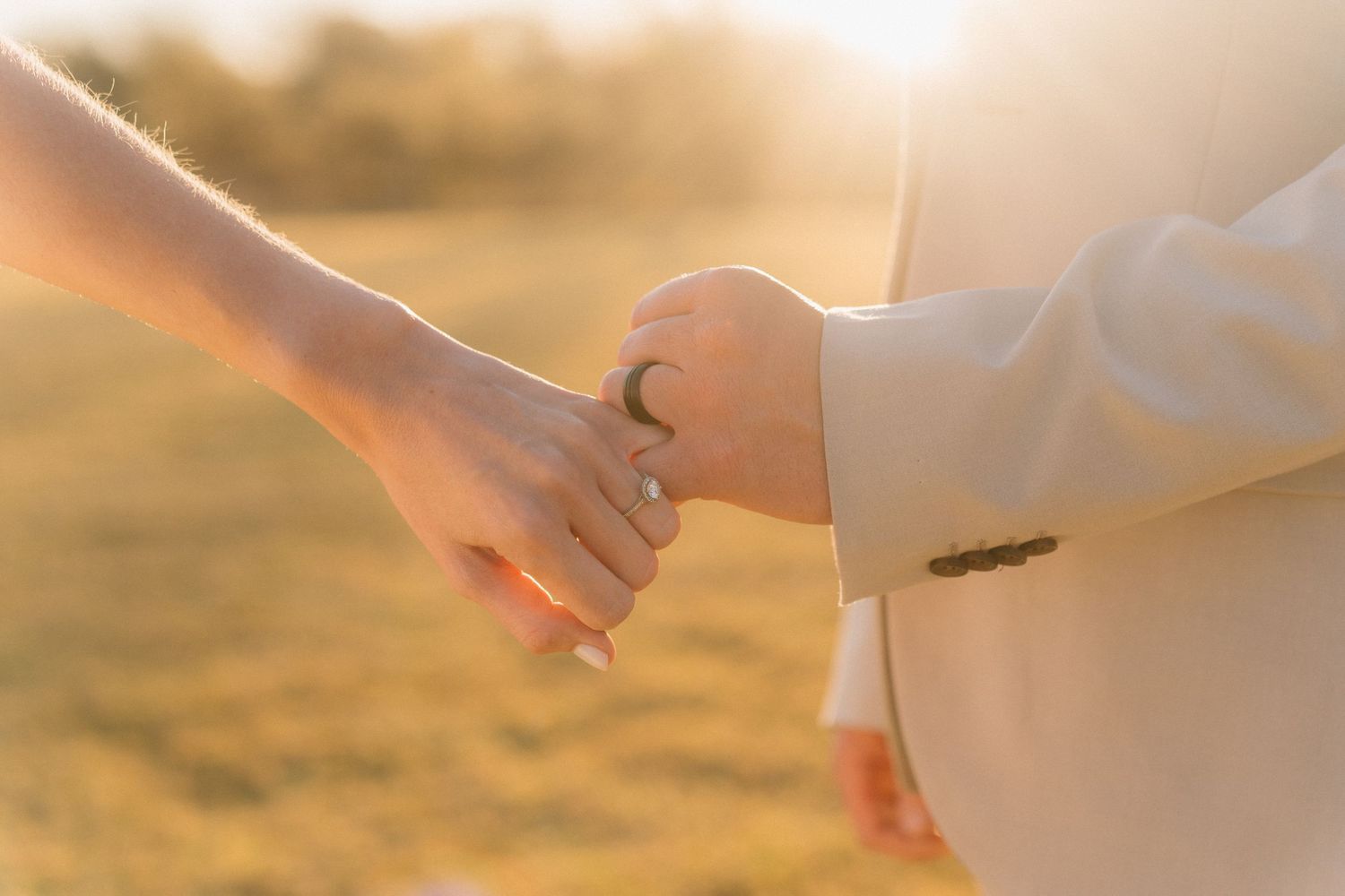 Two hands gently holding each other against a warm sunset background with golden sunlight glowing through.