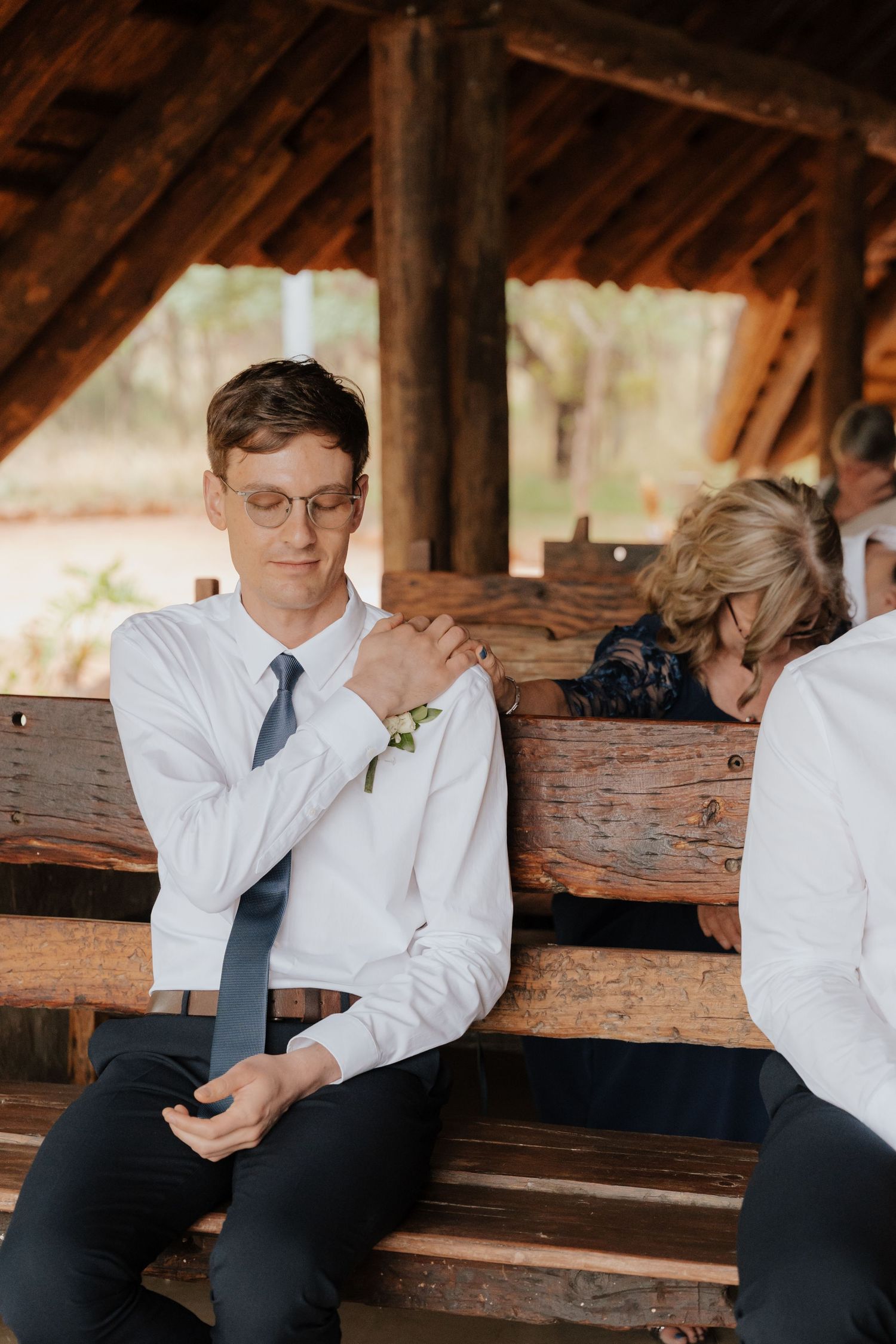 Wedding party member relaxing on rustic wooden bench.
