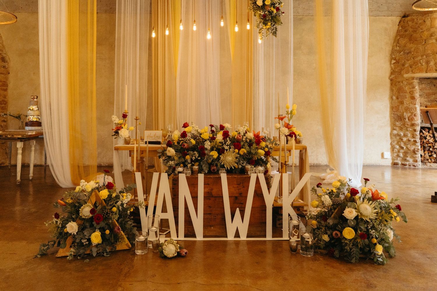 Wedding decor featuring 'VAN WYK' lettering surrounded by lush floral arrangements in pink and yellow.