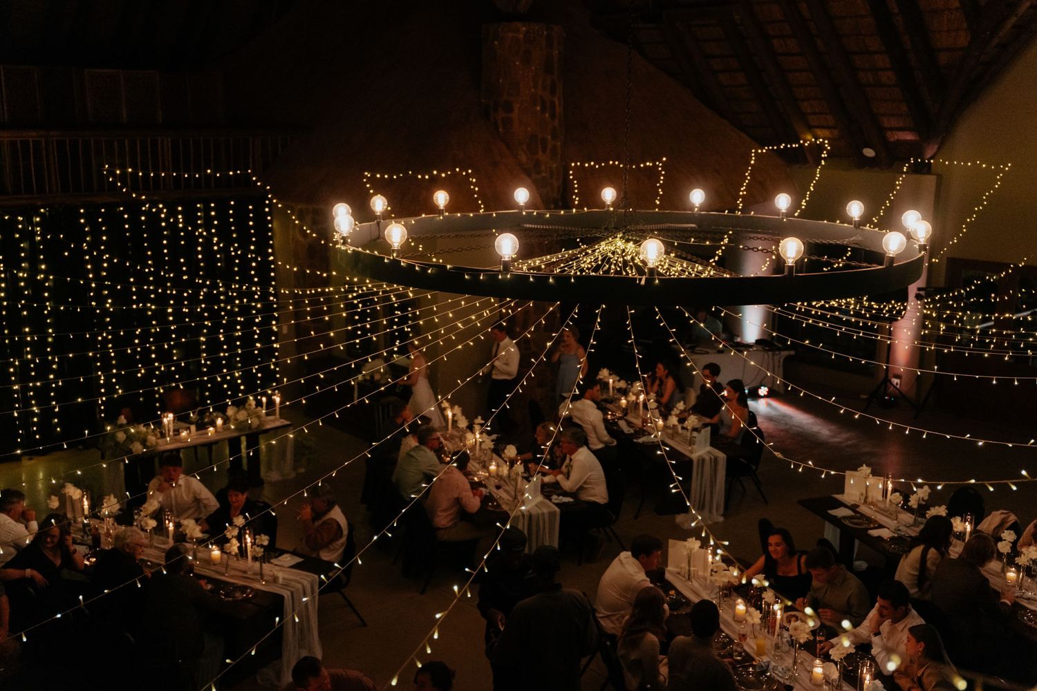 String lights create a magical ambiance in a dark reception venue with long dining tables.