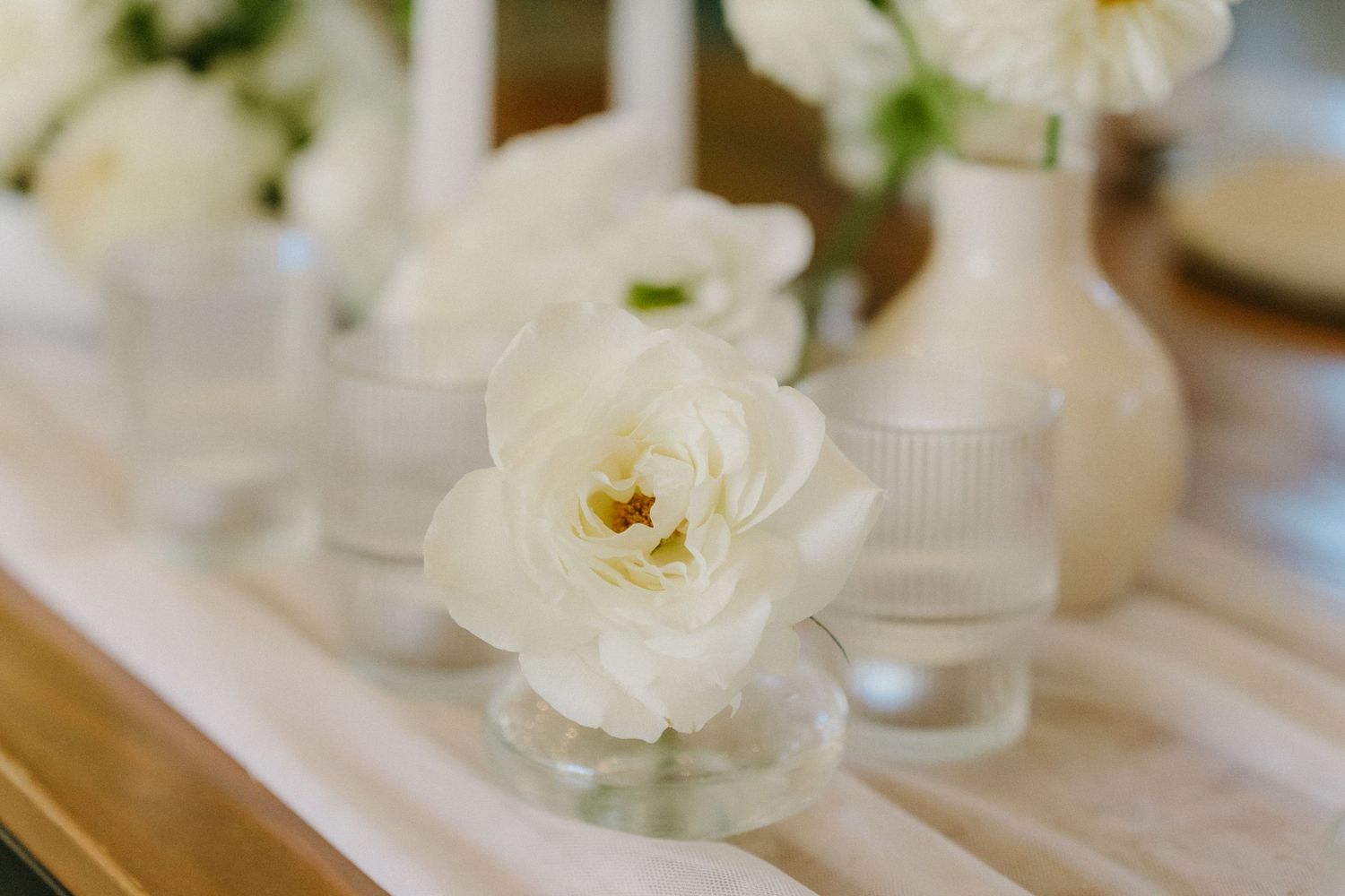 White gardenia flower in small glass vase with soft focus detail and clean minimalist styling on wooden table.