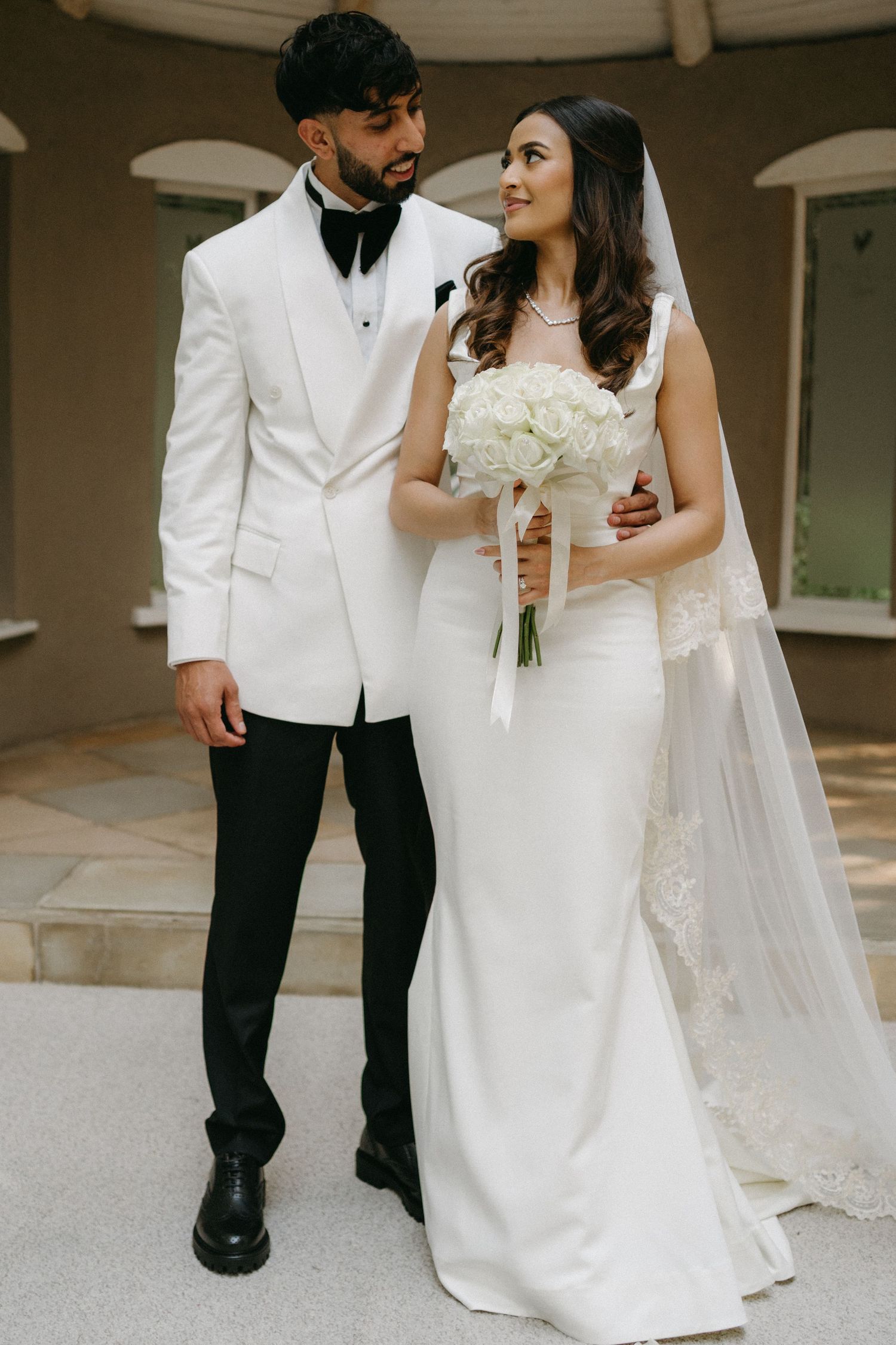Stylish couple in white and black formal attire posing for wedding photos.