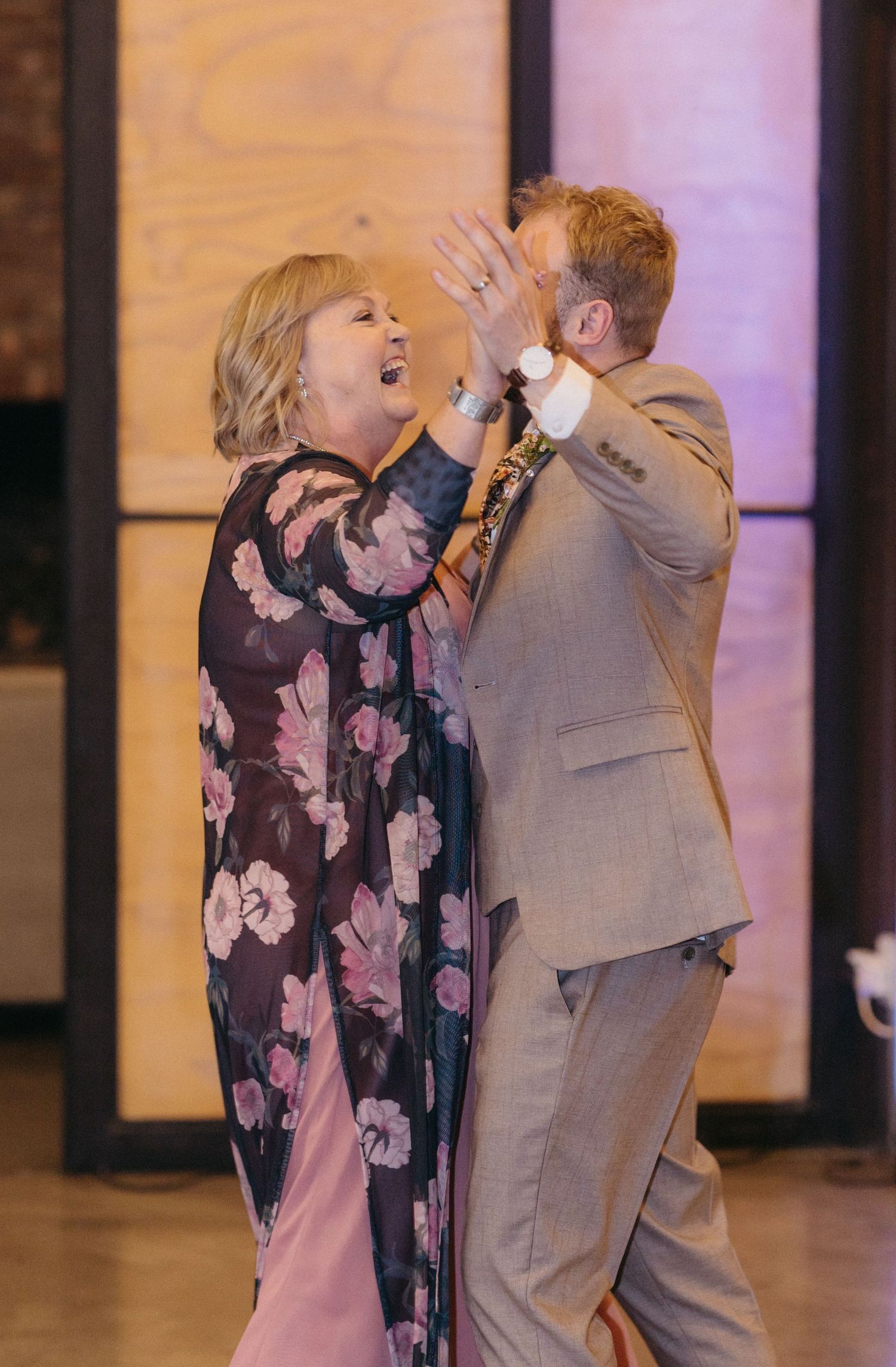 Two people in formal attire share an energetic celebration moment while dancing at an indoor event.