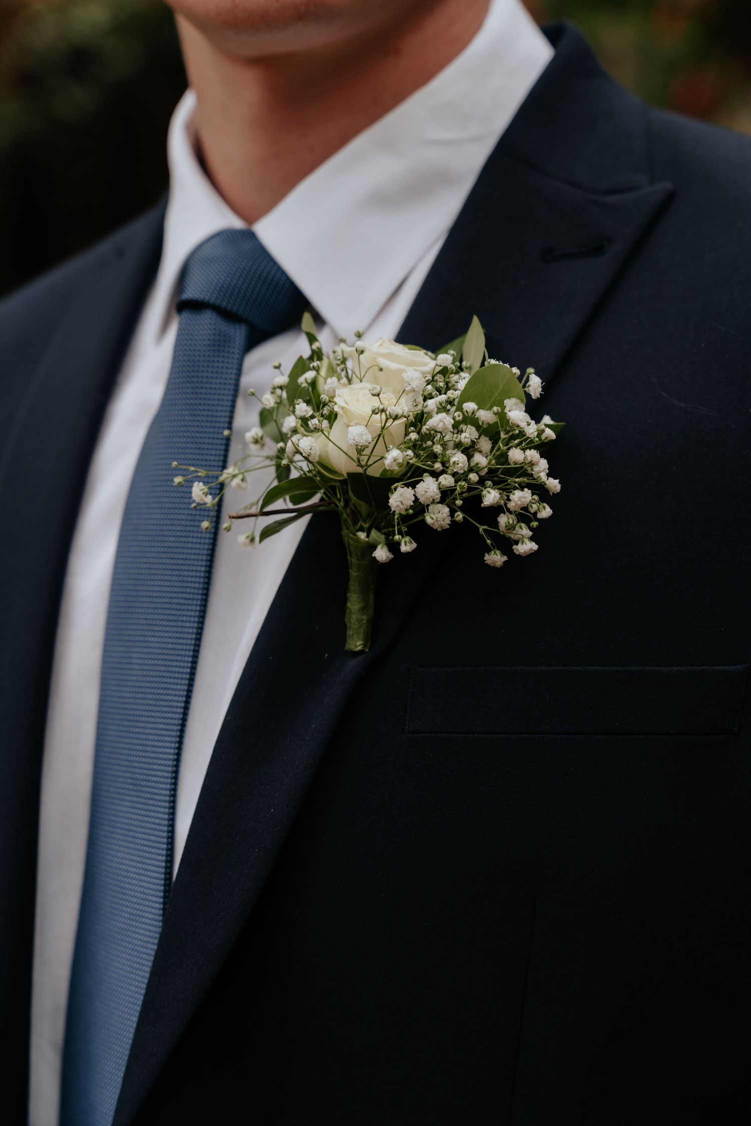 Close-up of a white rose and baby's breath boutonniere pinned to a navy suit lapel.