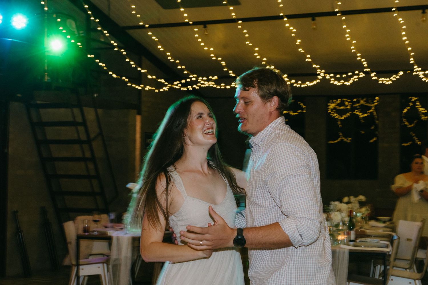 A couple shares a romantic dance moment under twinkling string lights at their wedding reception.