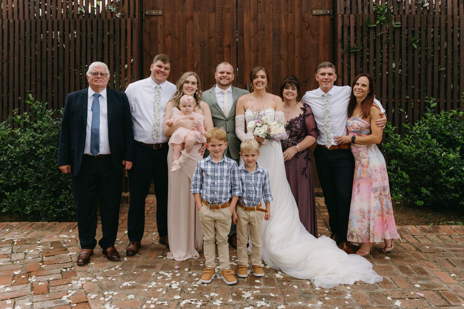 Wedding party and family members gathered for a formal group photo against wooden wall backdrop.