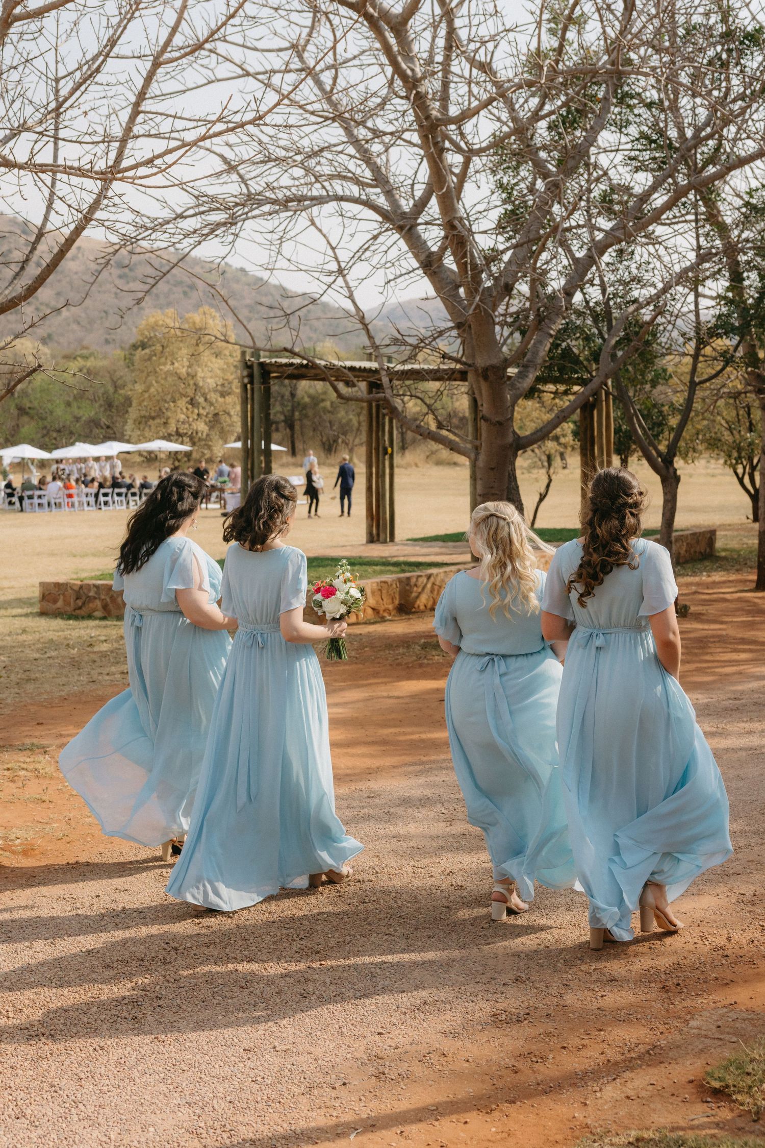 Bridesmaids in flowing light blue dresses twirl and dance outdoors.