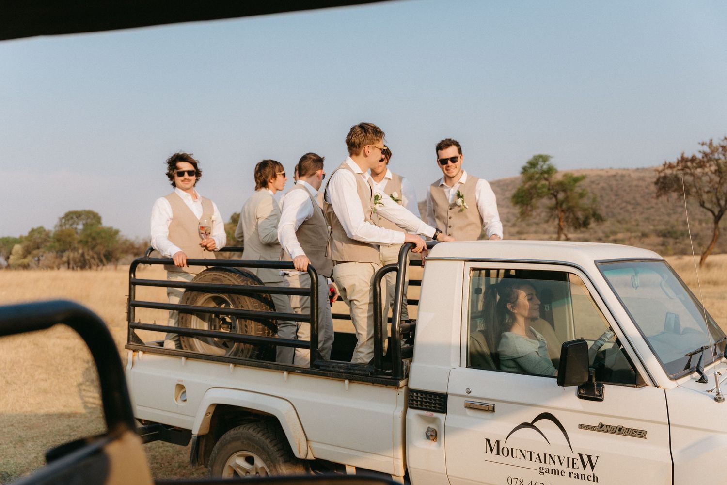 Wedding party guests gathered around white pickup trucks in an outdoor setting.