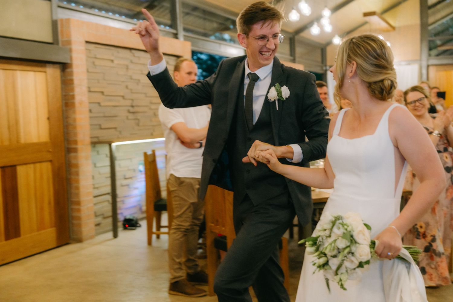 A couple celebrates with joyful dancing at their wedding reception as guests watch in the background.