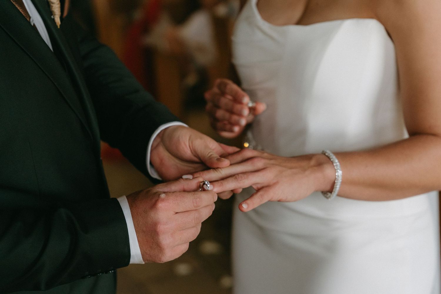 Close-up detail of hands exchanging wedding rings during ceremony.
