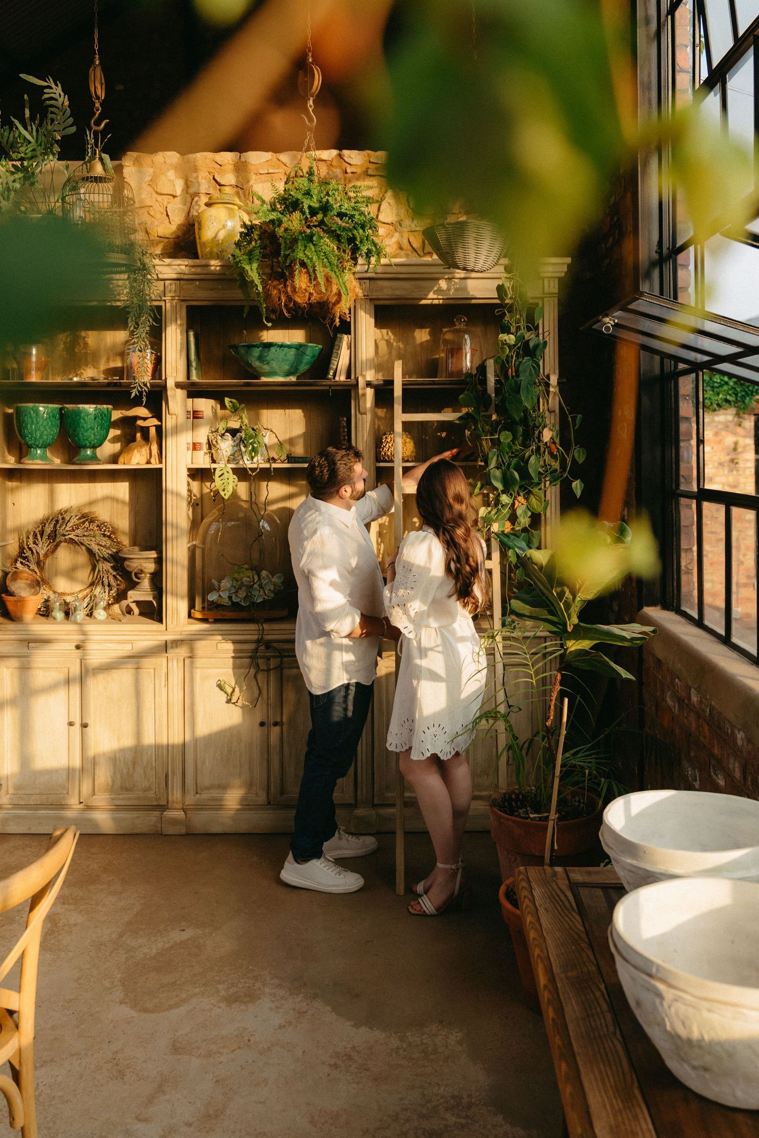 Sunlit greenhouse interior with white bathtubs and potted plants creating a serene spa-like atmosphere.
