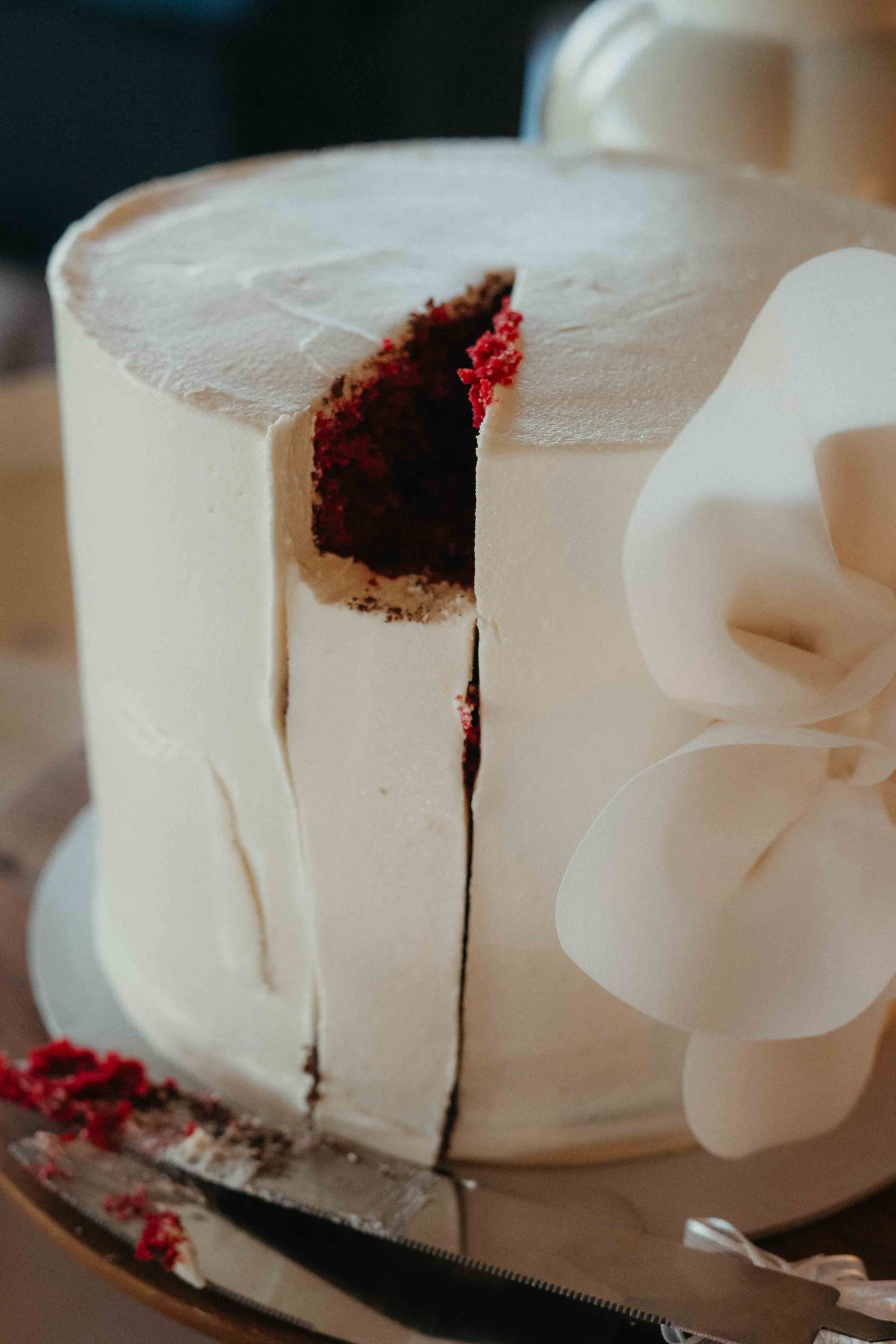 Red velvet wedding cake with white frosting and bow decoration, sliced to reveal dark interior layers.