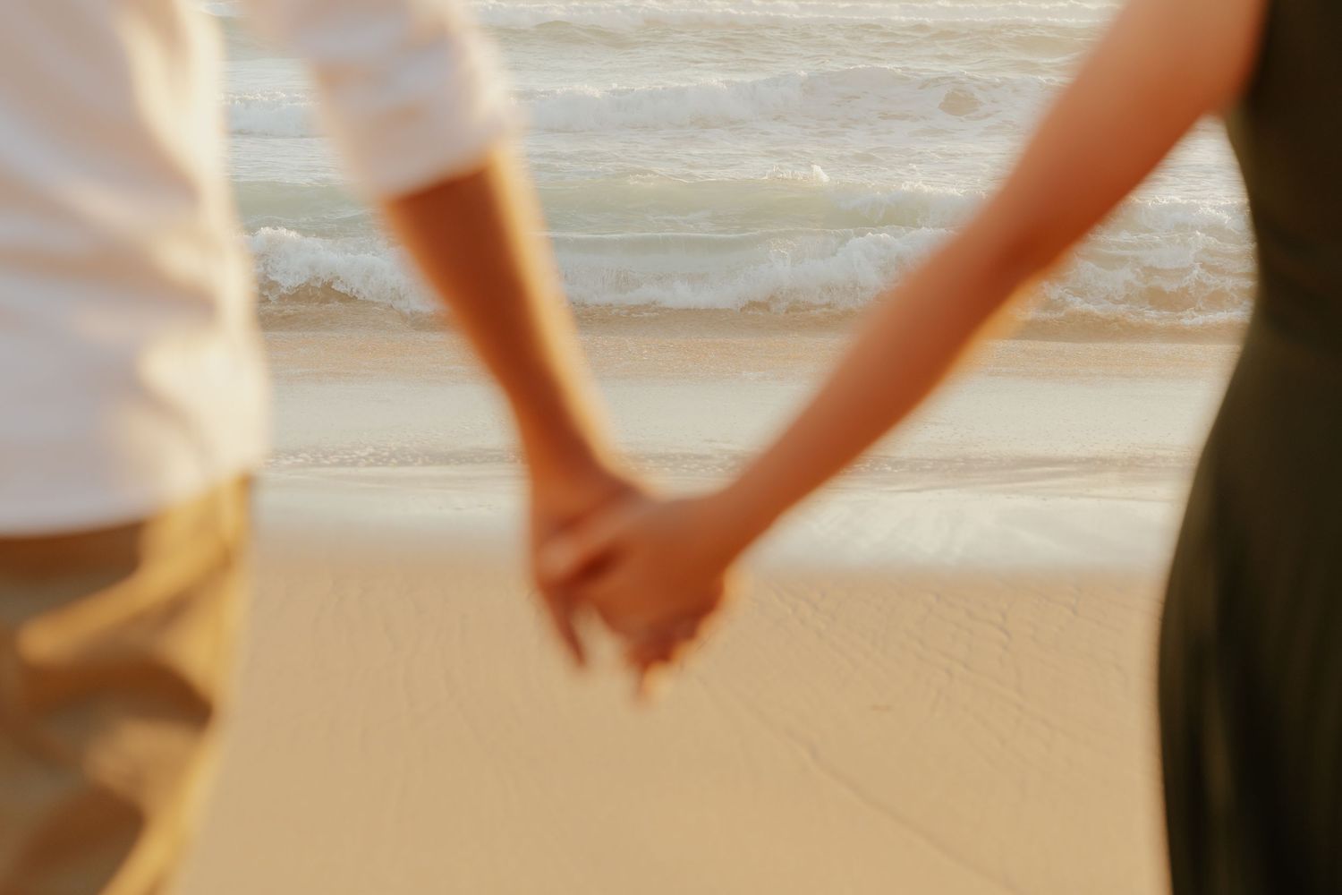 A couple holds hands while walking barefoot along a sandy beach at sunset in the Western Cape, South Africa