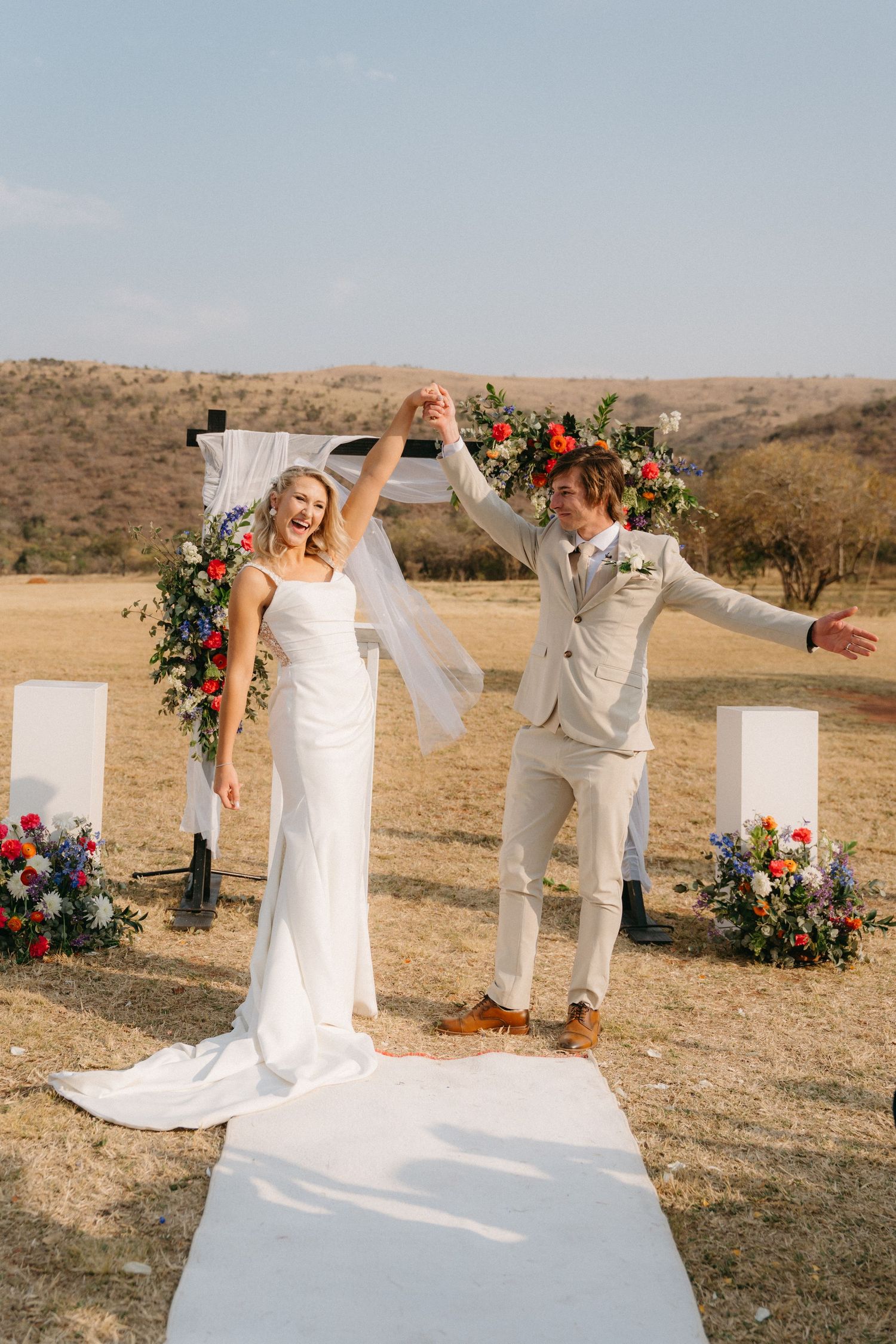 Wedding ceremony setup in a desert landscape with white pillars and floral arrangements framing the altar area.