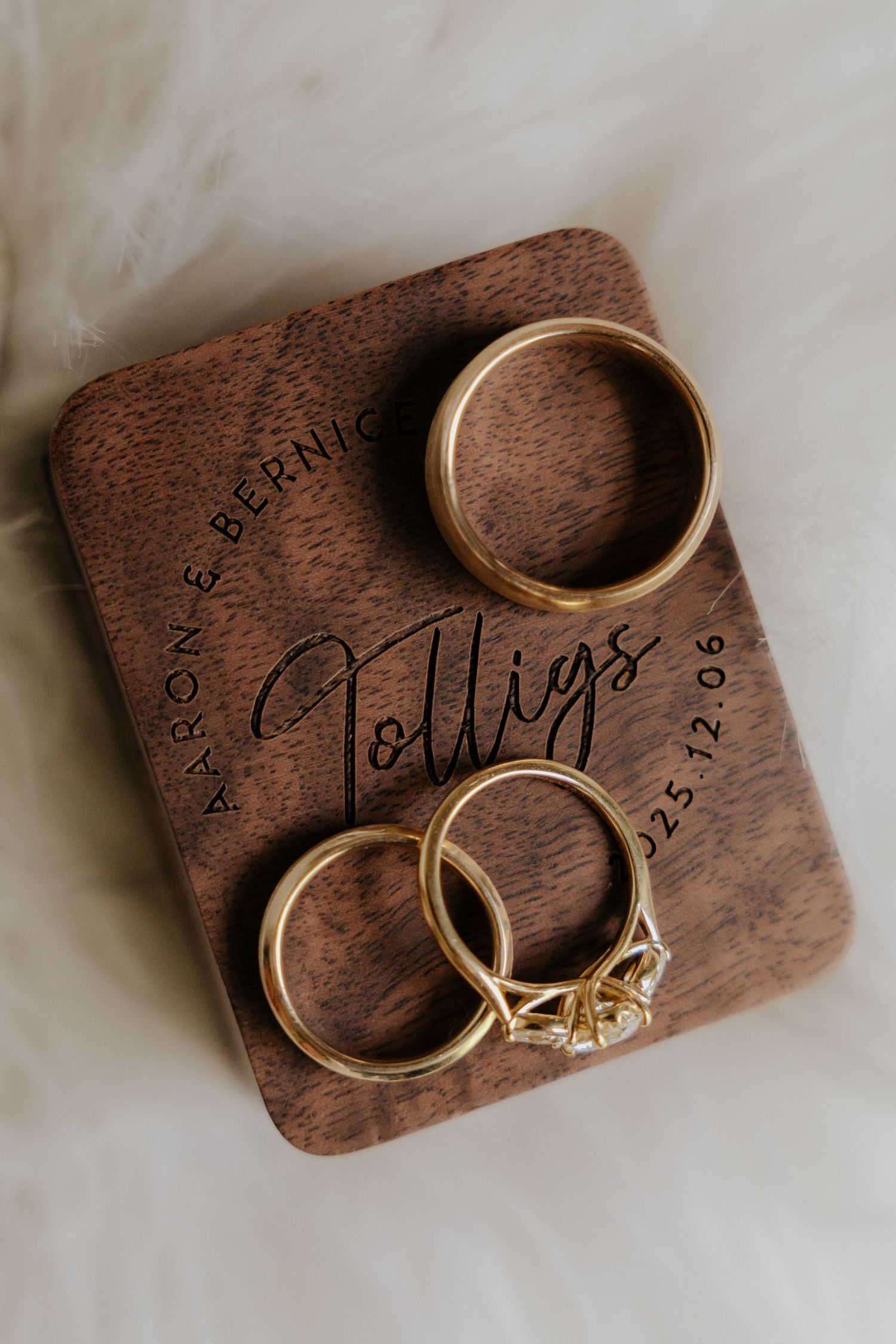 Custom wooden ring box with engraved text and gold wedding bands displayed on white surface in multiple angles.