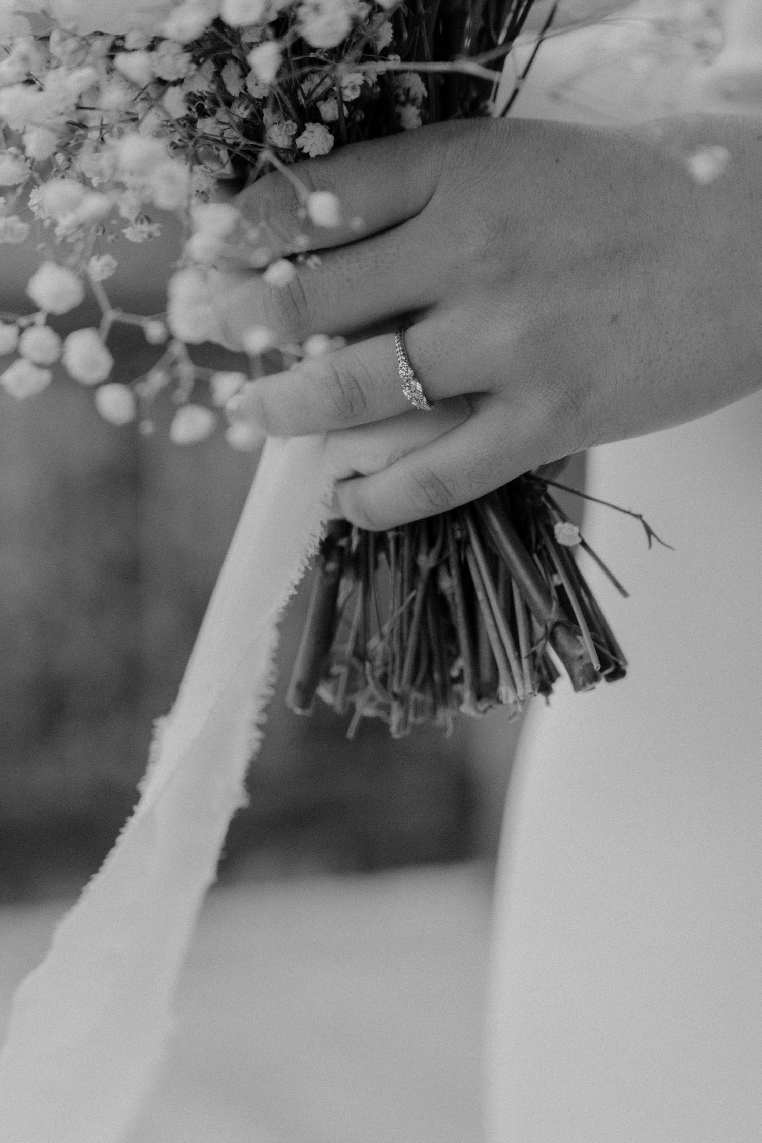 Black and white close-up of hands holding a wedding bouquet wrapped in white ribbon.