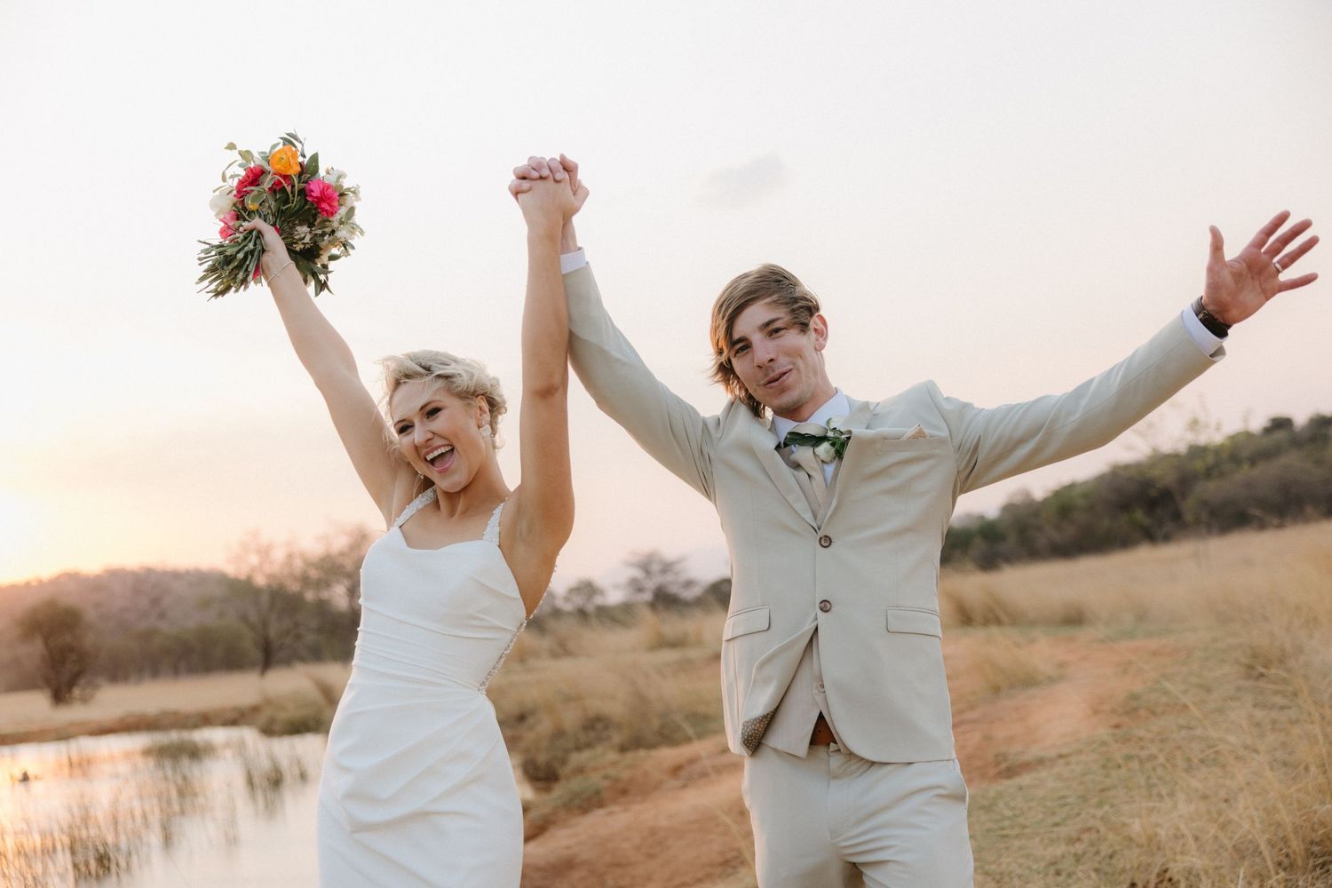Joyful newlyweds celebrate with raised arms against a sunset backdrop.