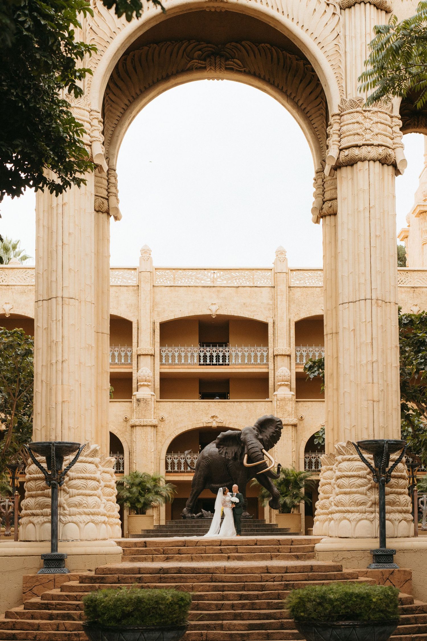 Elegant wedding ceremony setting with a majestic stone archway and elephant statue on circular steps at a grand venue.