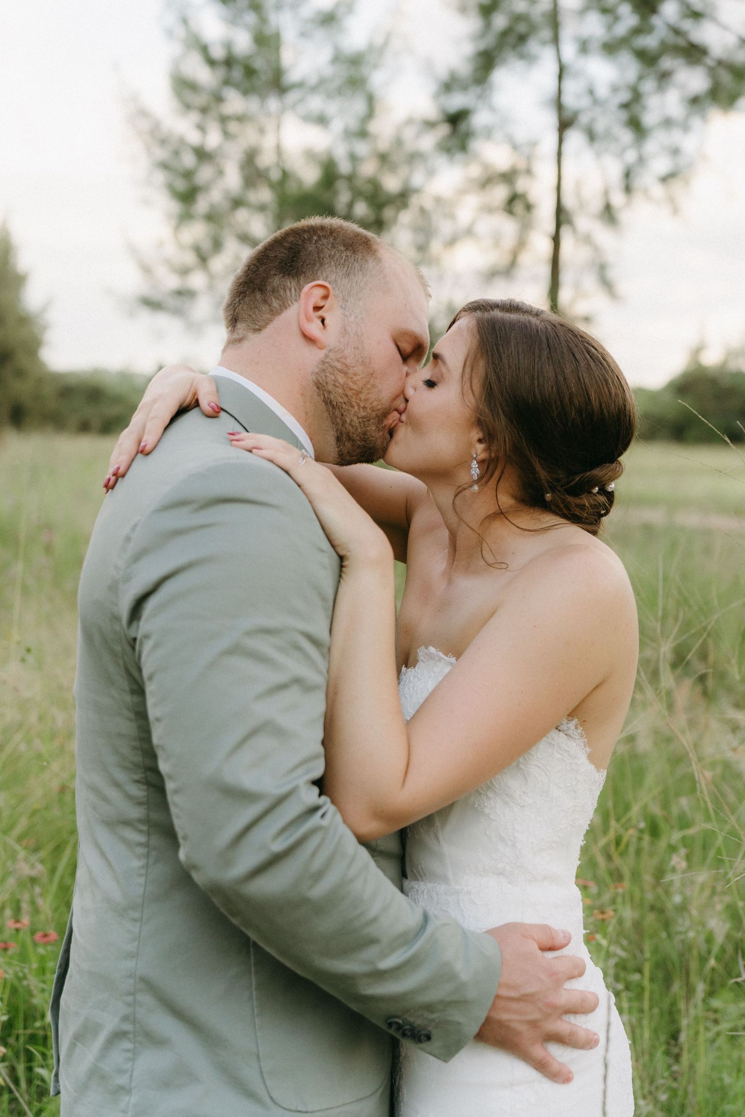 A tender moment between newlyweds sharing a kiss in a grassy field on their wedding day.