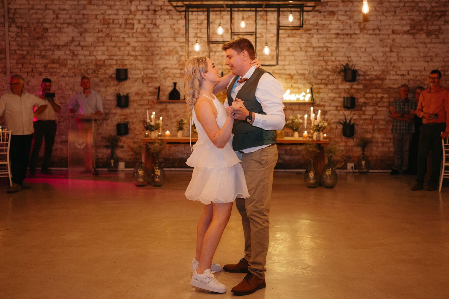 Wedding couple dancing in an intimate brick-walled venue with warm lighting and romantic atmosphere.