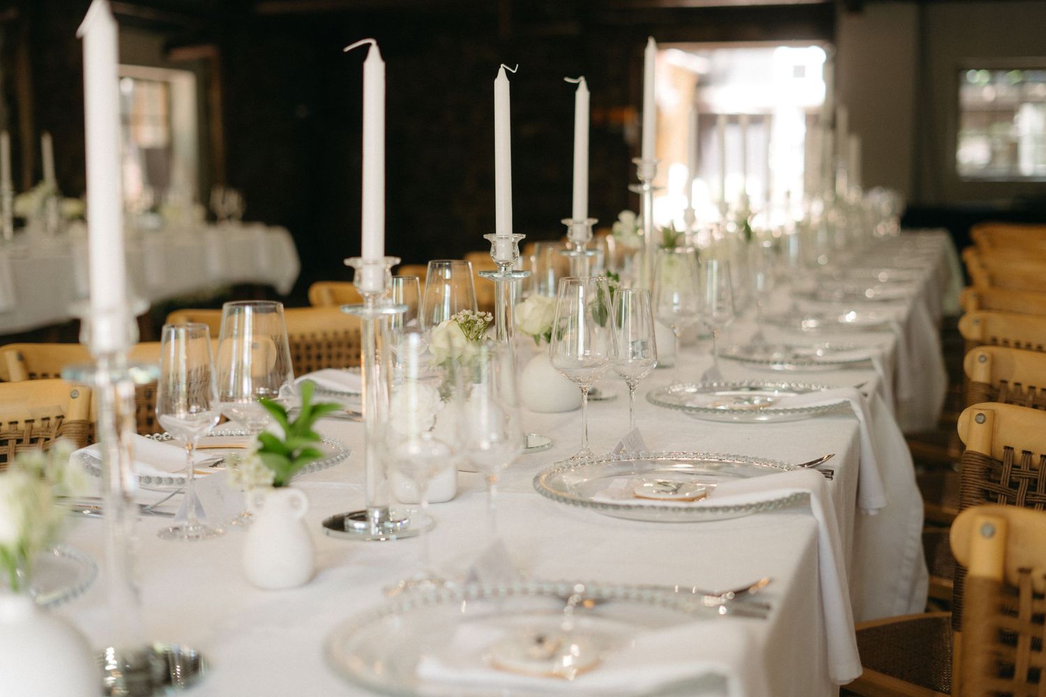 Elegant wedding reception table setting with white candles, glassware and natural elements on a crisp white tablecloth.