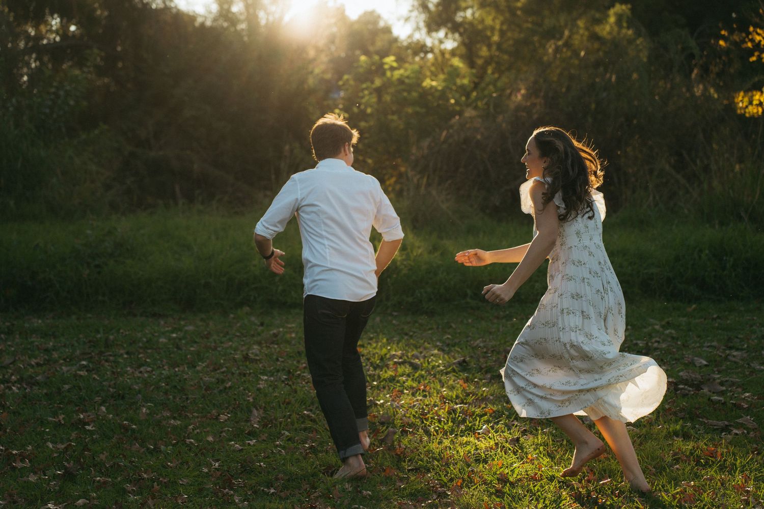 A couple walking through a meadow reaching for each other's hands.