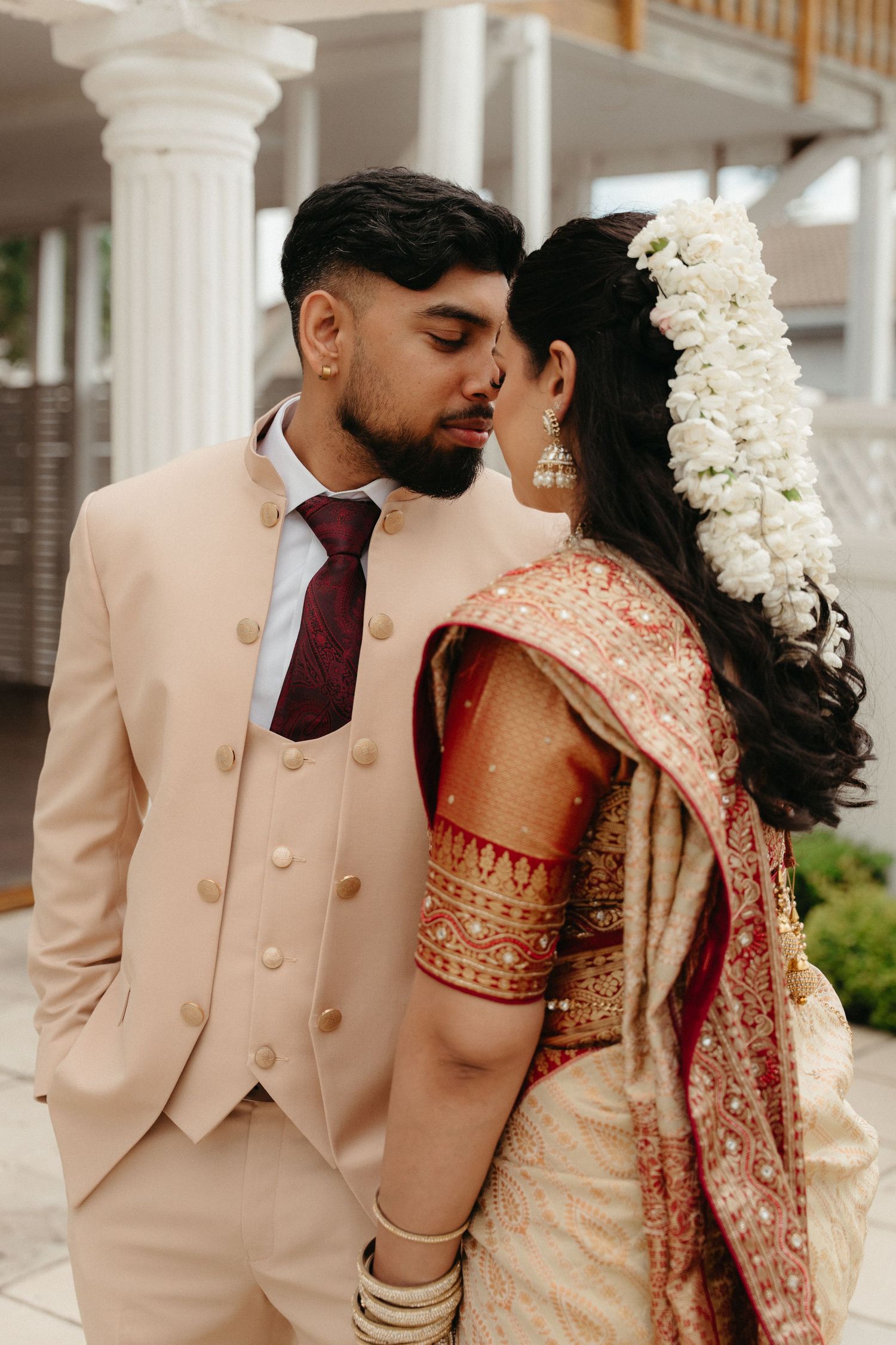 Couple in traditional Indian wedding attire share intimate moments in elegant cream and burgundy outfits.