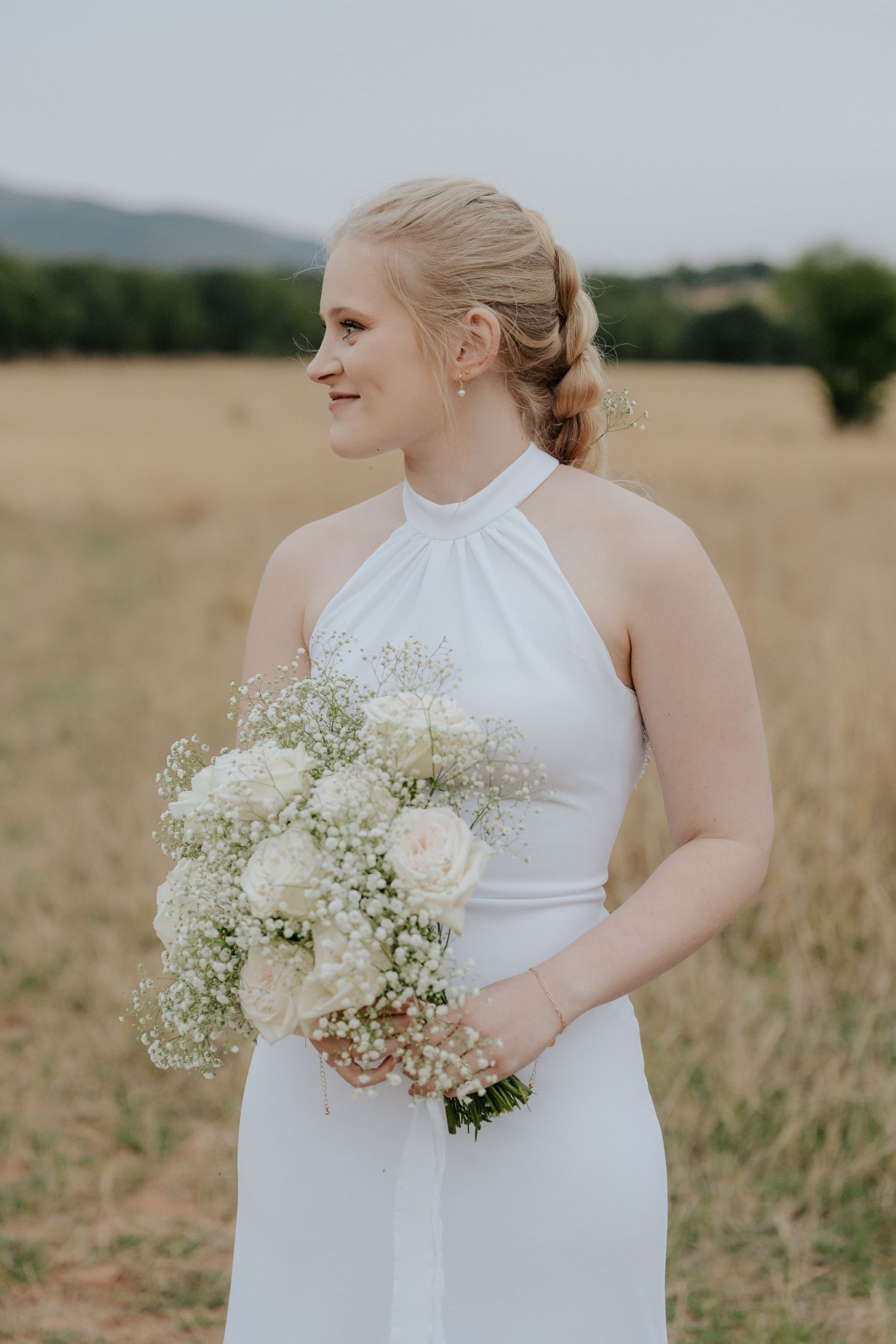 Person in white wedding dress holding baby's breath bouquet poses in a golden field at sunset.