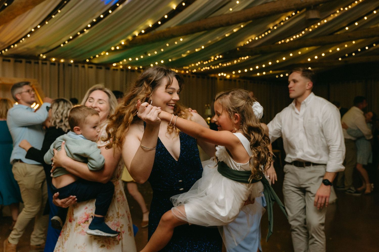 Wedding guests dancing together under warm string lights during reception celebration.