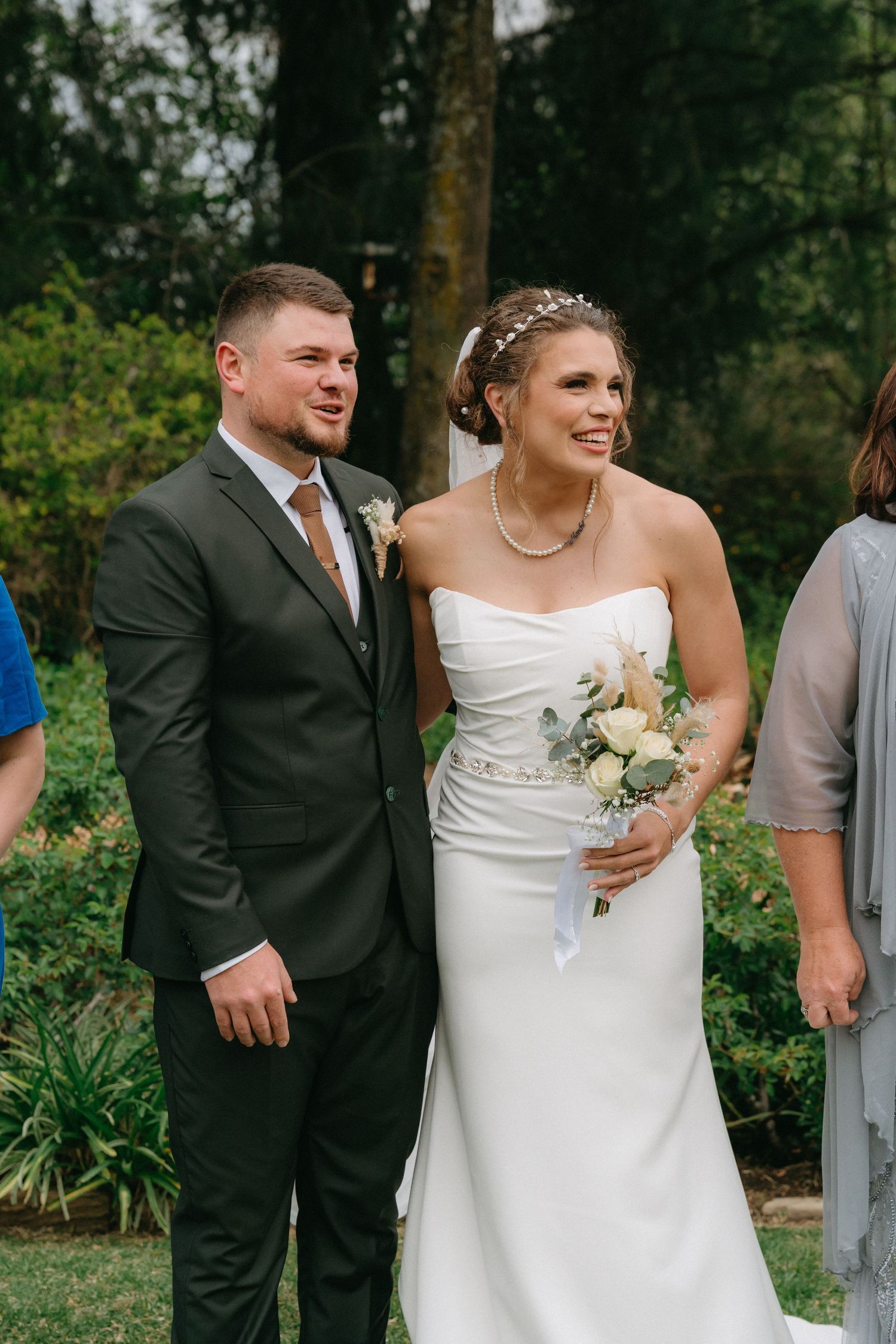 Wedding party in formal attire walking and laughing together outdoors on a grassy lawn.