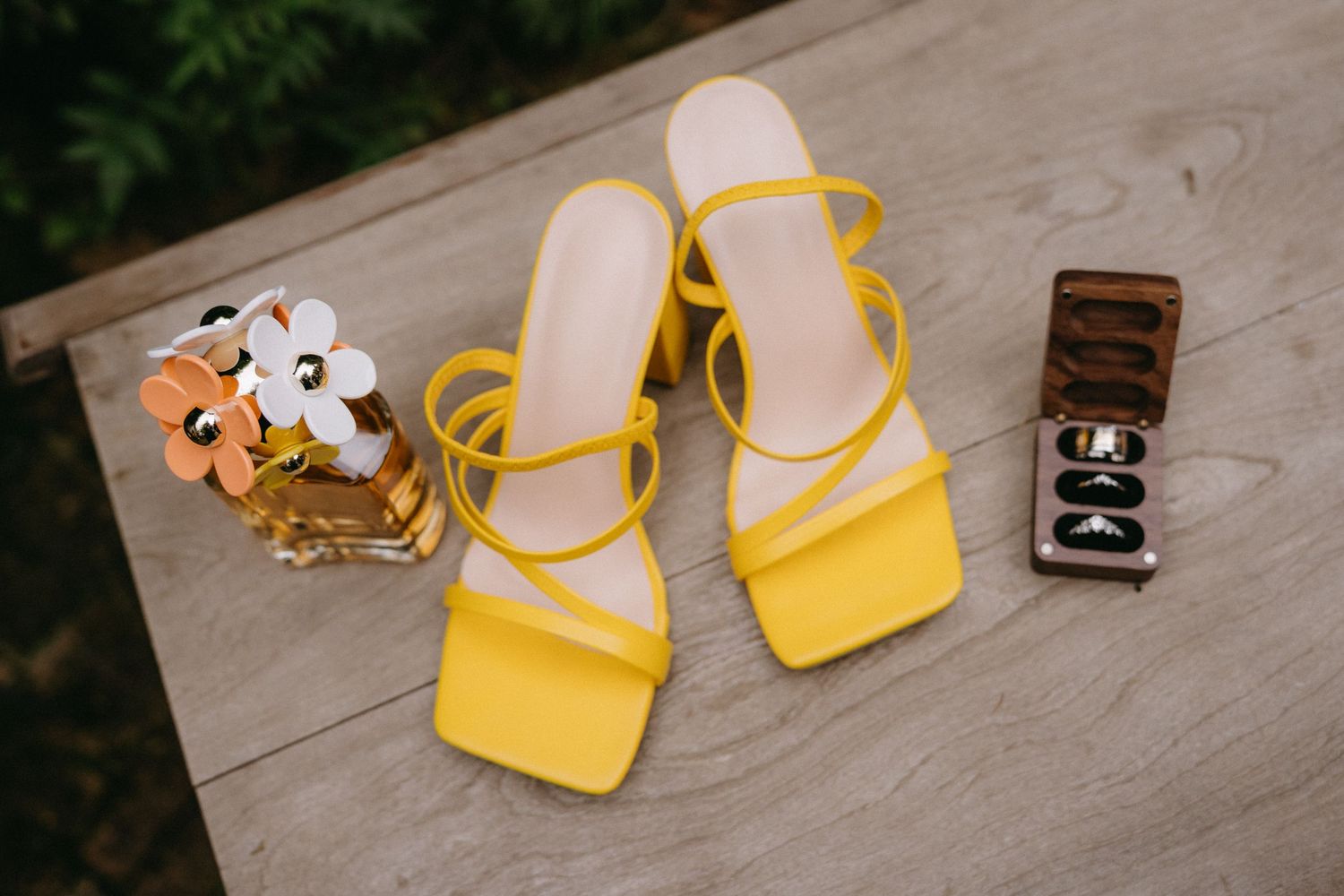 Yellow strappy sandals with wedding accessories arranged on wooden surface.