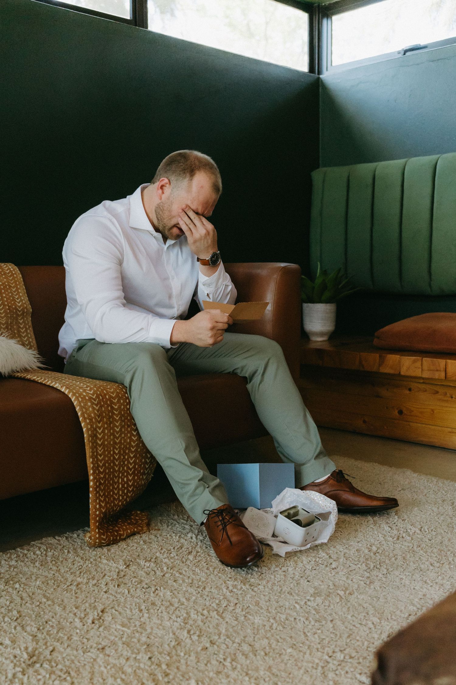 Person in light shirt sitting on woven chair appears distressed while covering face in dark room with carpet.