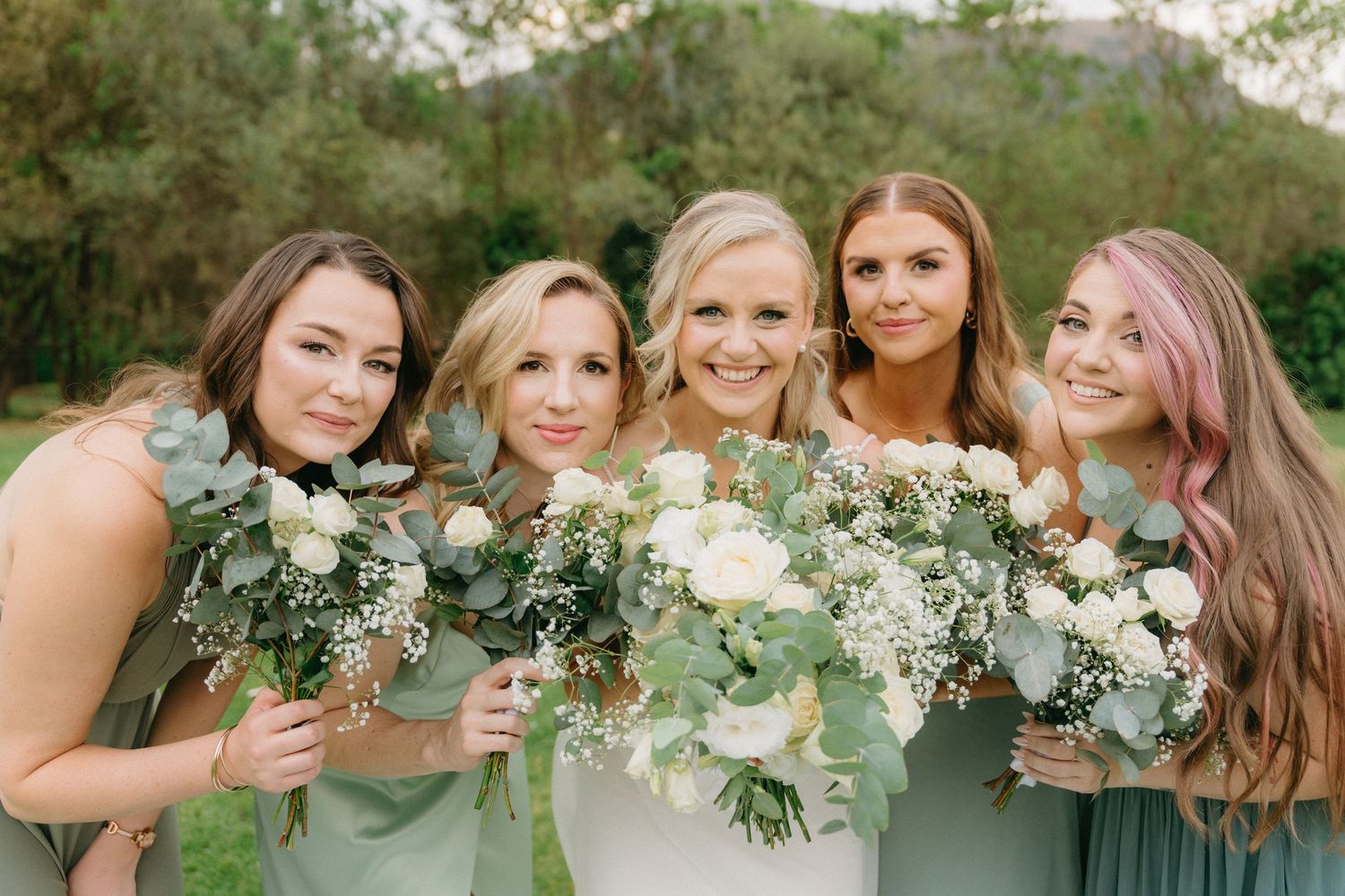 Bridesmaids in sage green dresses hold elegant white floral bouquets.