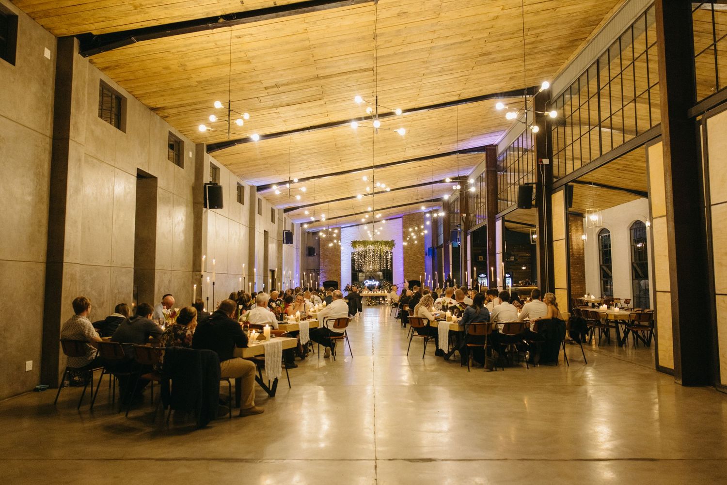 Elegant wedding reception venue with long tables and purple uplighting in a historic hall with high ceilings.