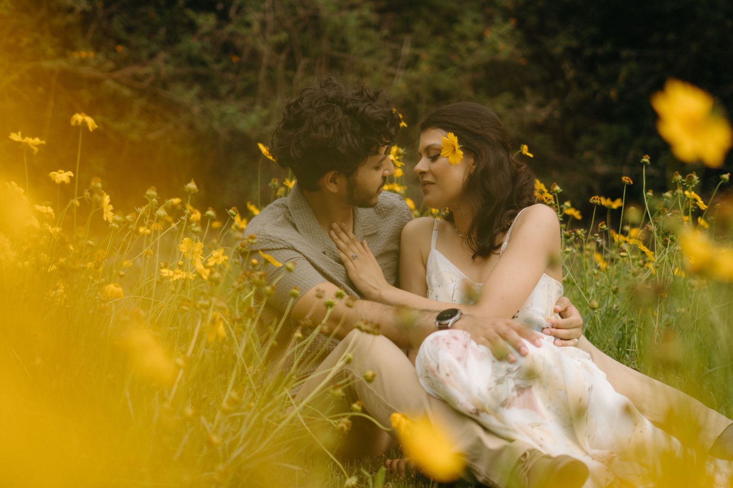 Romantic couple sharing an intimate moment in a field of yellow wildflowers during golden hour.