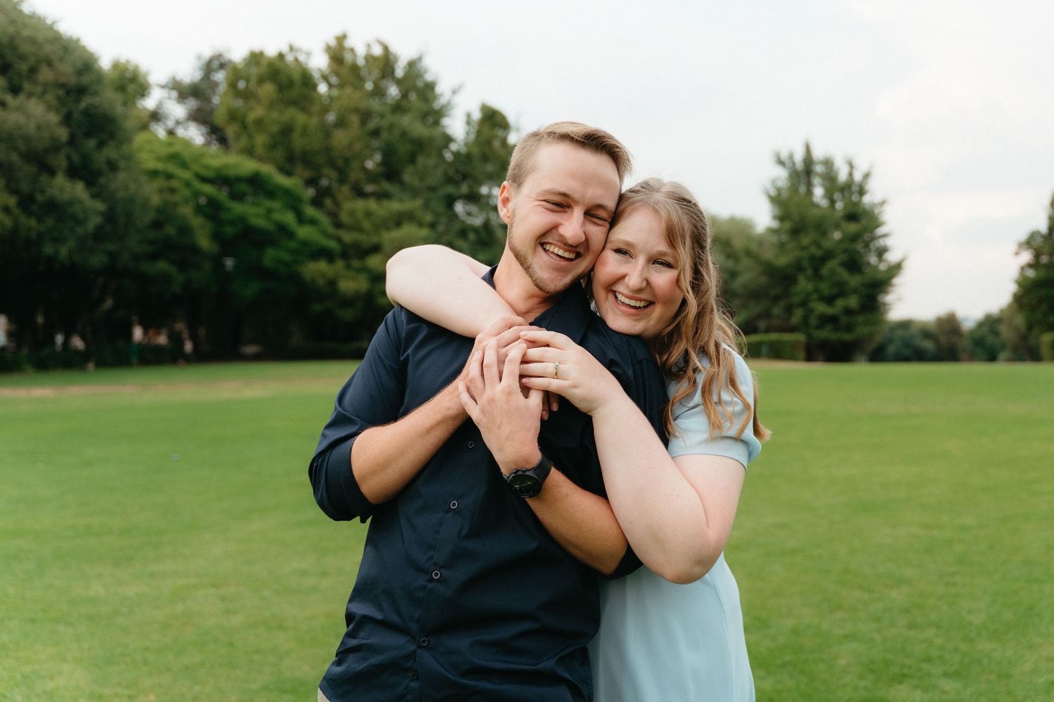 A couple shares joyful moments together in a grassy park setting during a photo session.