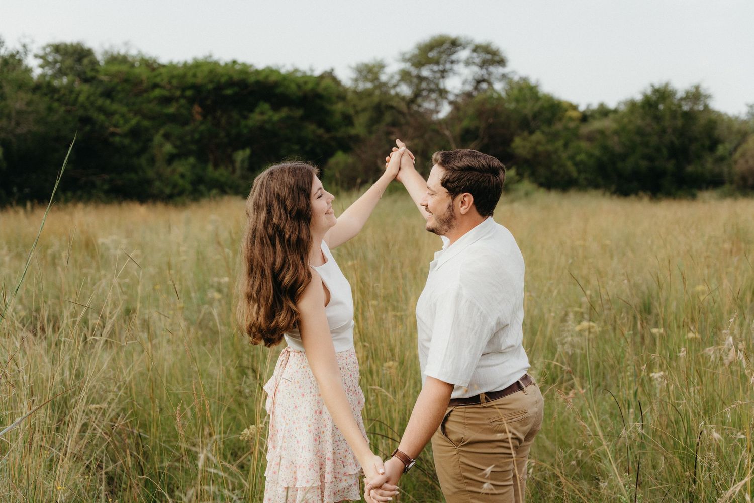 Couple dancing in a field of tall grass, woman touching man's face, surrounded by lush green trees.