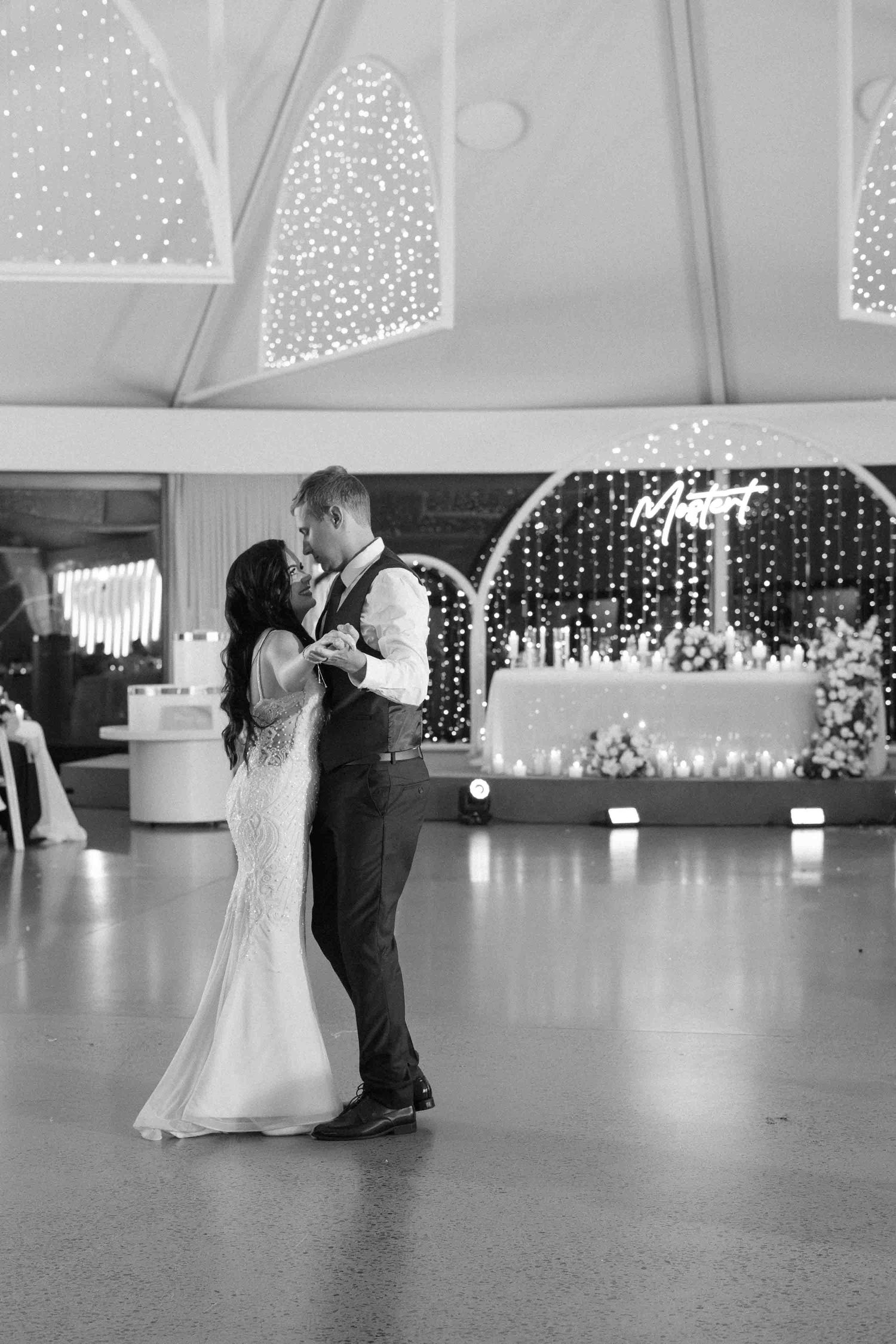 Bride and groom share their first dance in an elegant venue adorned with fairy lights in black and white.