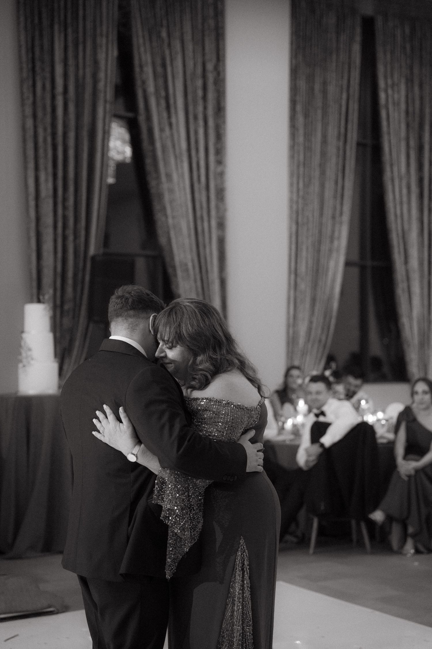 Black and white photo of a groom and his mother sharing an emotional dance at a wedding reception.