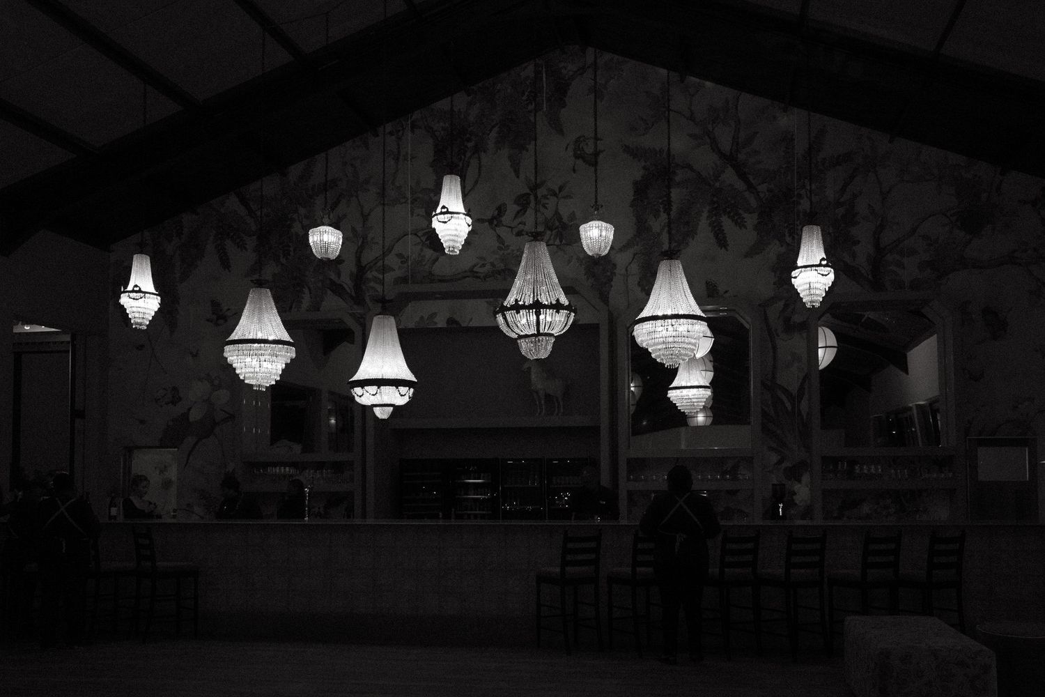 Black and white photo of elegant chandeliers illuminating a dark wedding venue interior with floral wallpaper in the Garden Route