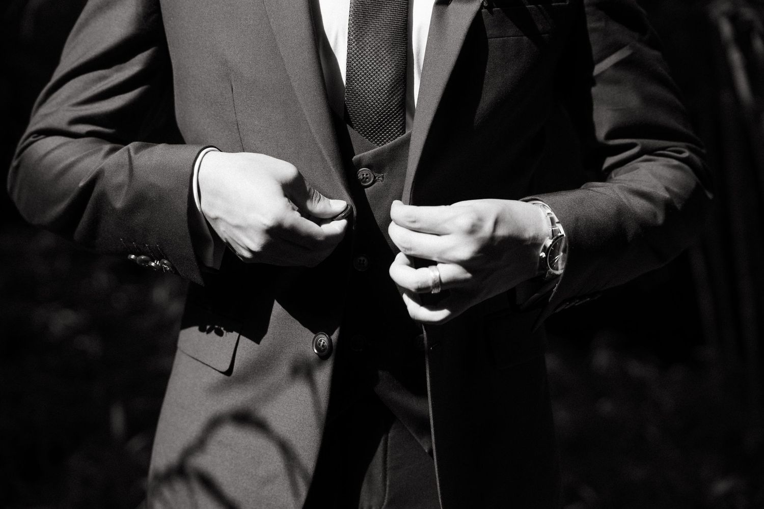 Black and white photo of two men in suits adjusting their jacket buttons, one wearing a watch.