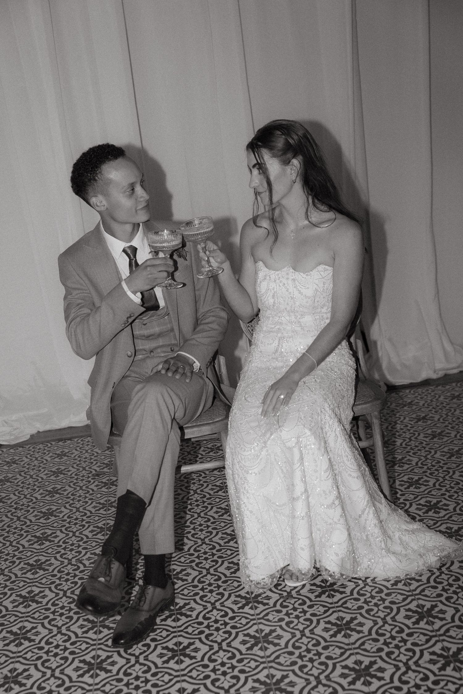 Black and white photo of a bride and groom toasting with champagne glasses at their wedding reception.