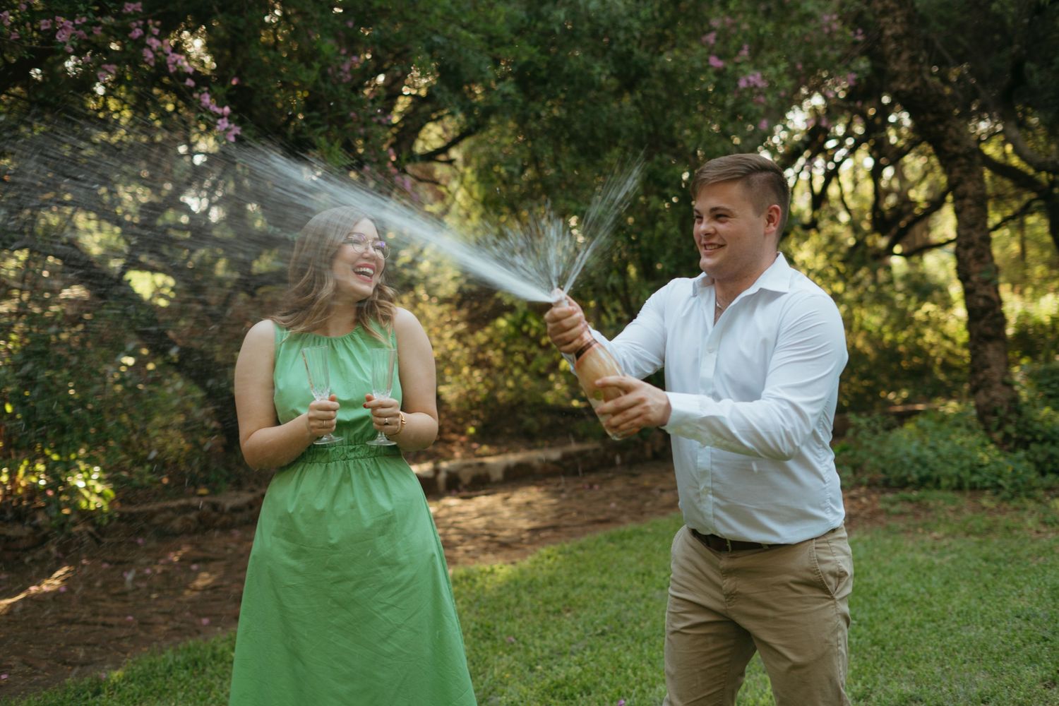A playful moment as champagne sprays during an outdoor celebration in a garden setting.