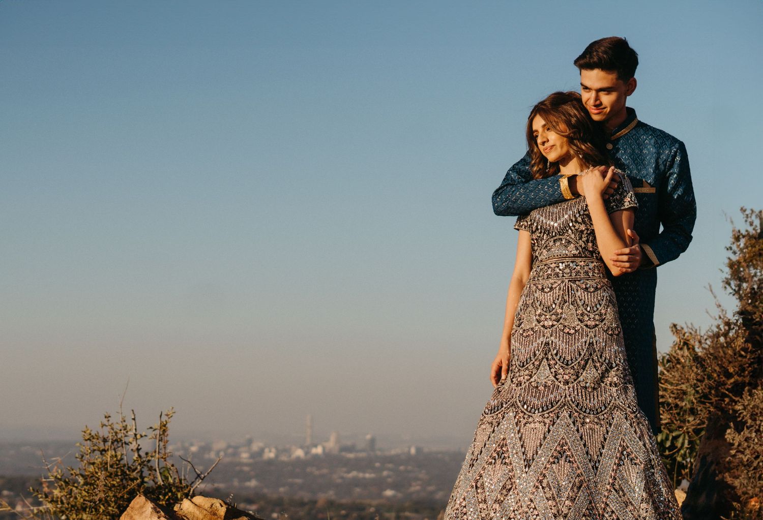 A romantic sunset embrace overlooking a distant city from a hilltop viewpoint.