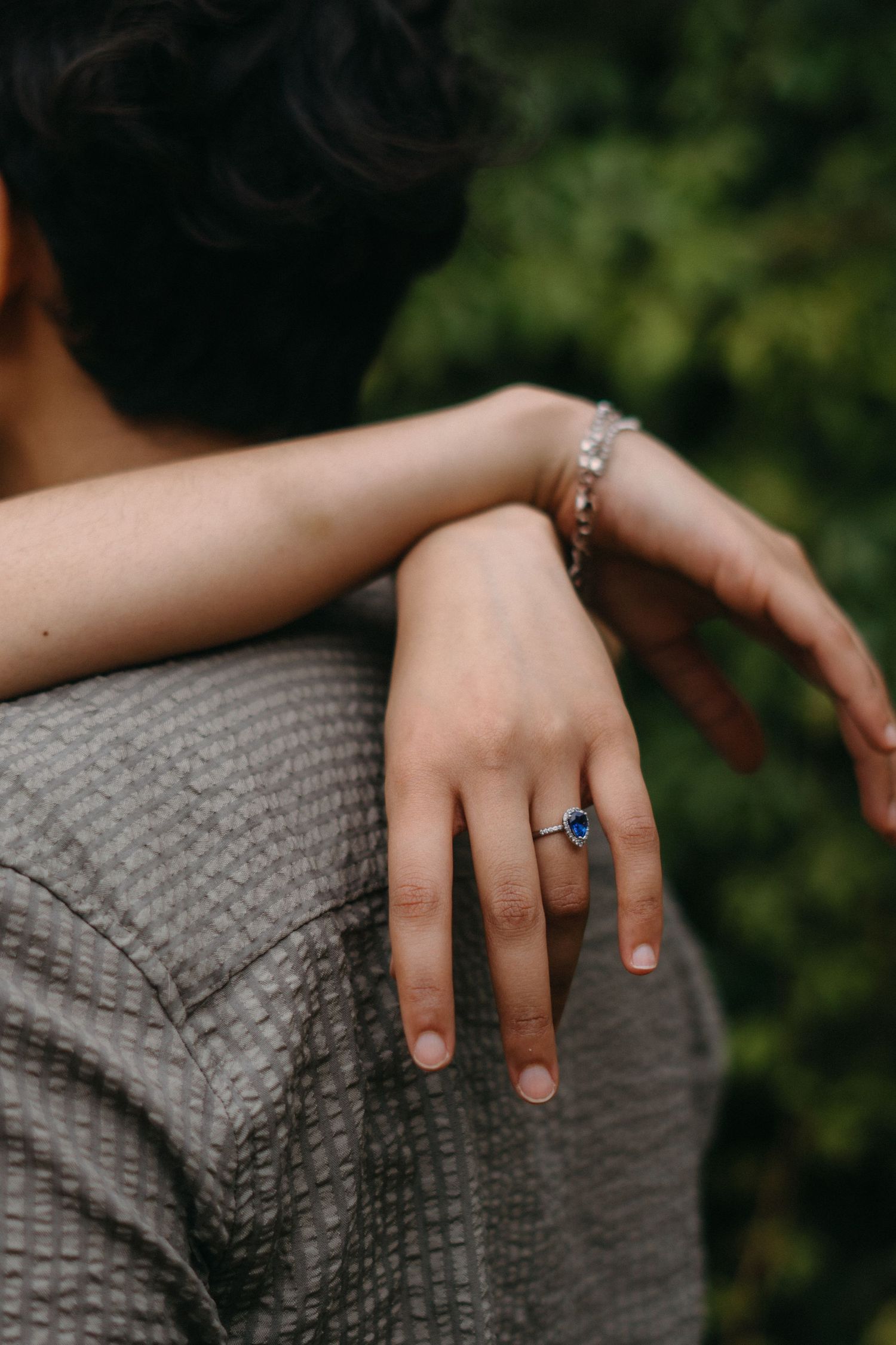Close-up of engagement ring and bracelet as couple embraces outdoors.