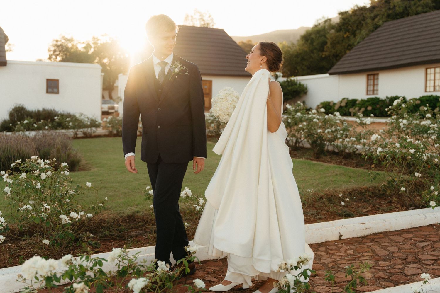 A romantic sunset wedding scene in a garden with white roses and stone pathways.