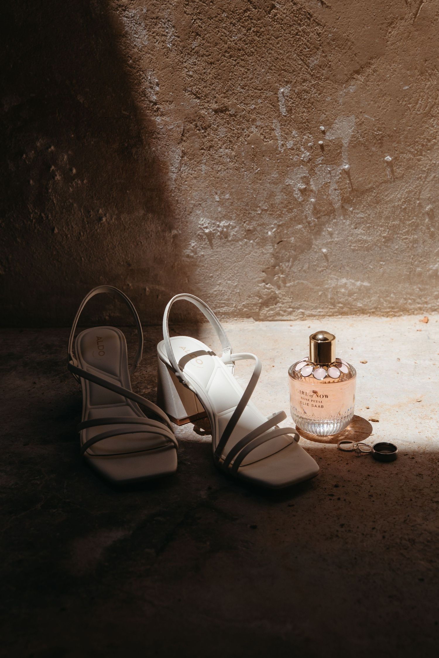 A pair of white ballet flats sits in dramatic lighting against a textured wall with scattered light and shadow effects.