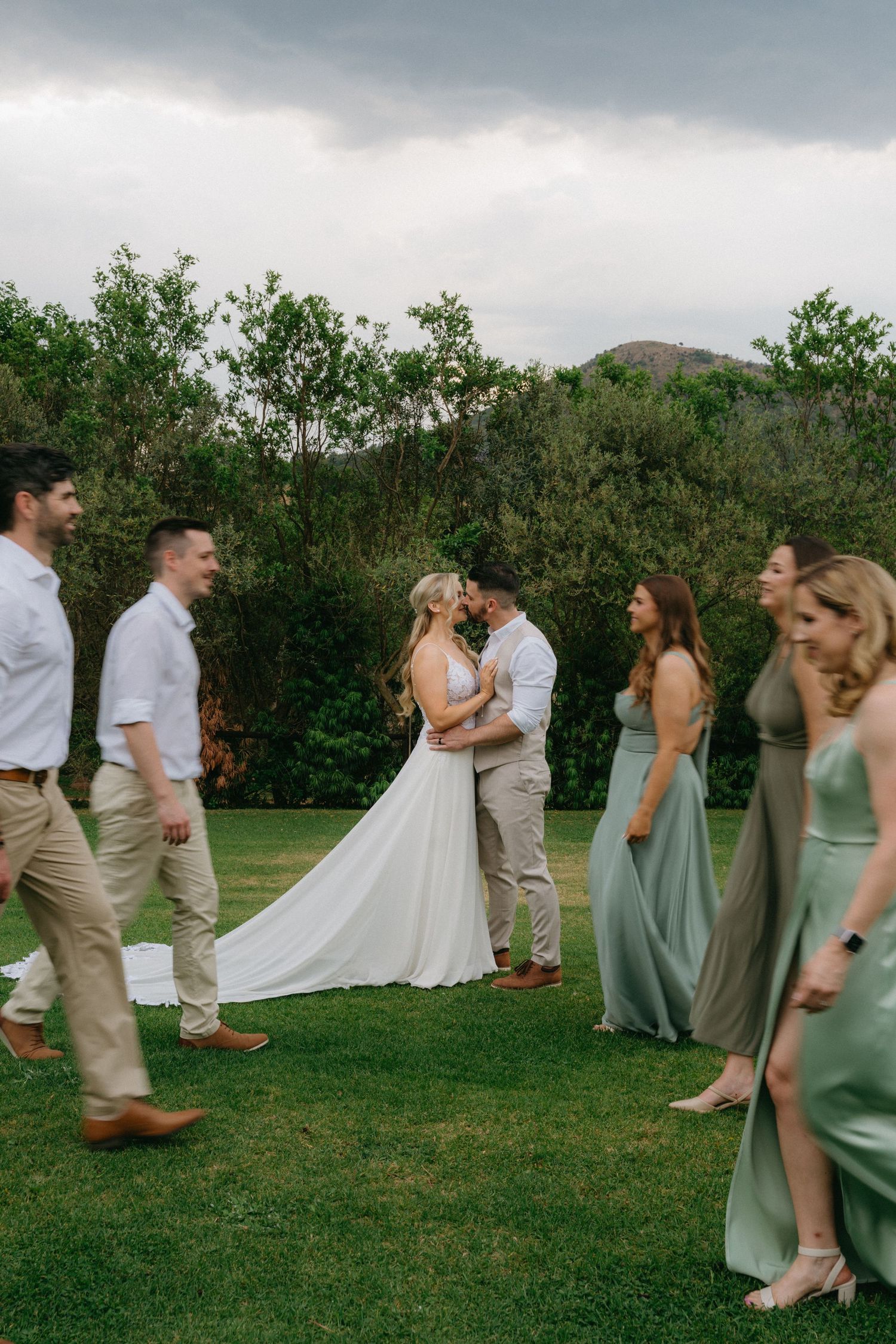 Wedding party in sage green dresses and khaki suits posing outdoors on a cloudy day.